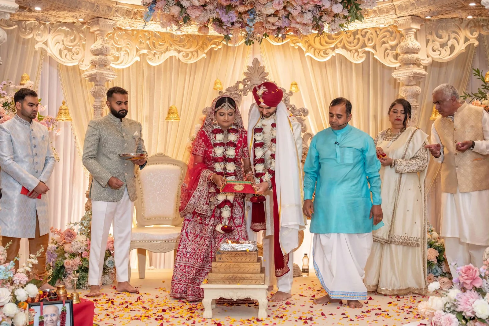 Bride and groom standing at the mandap surrounded by family, petals across the floor