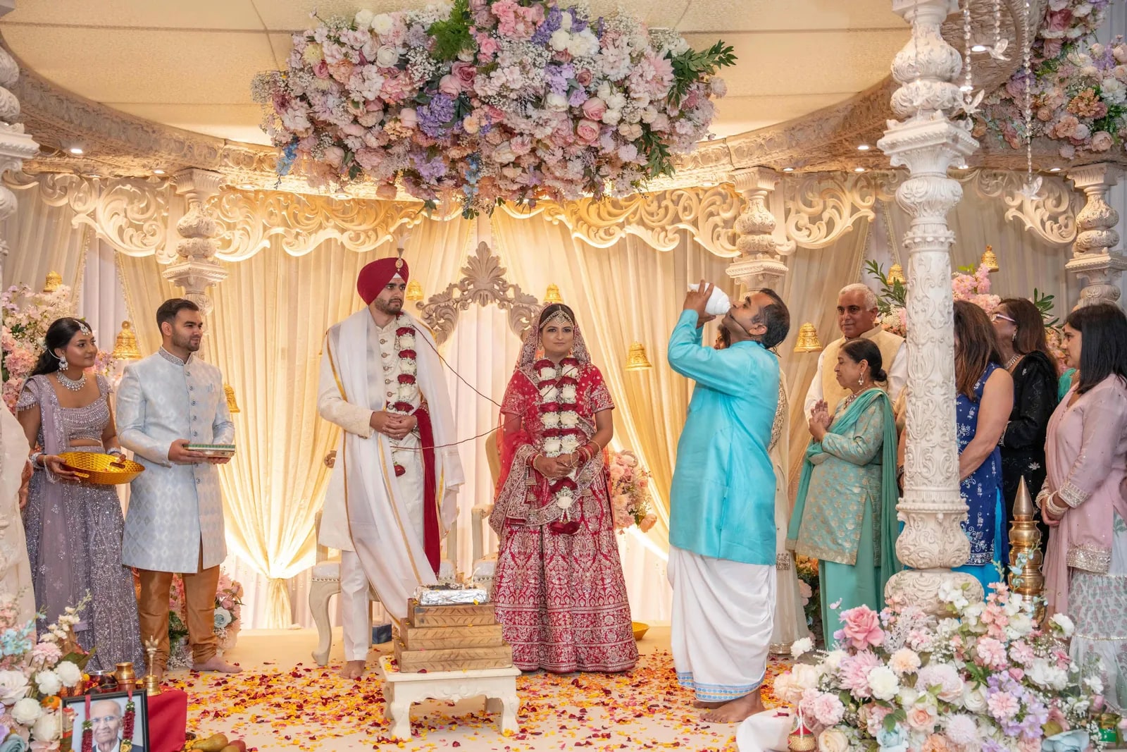The couple at the mandap during the ceremony, family gathered on both sides
