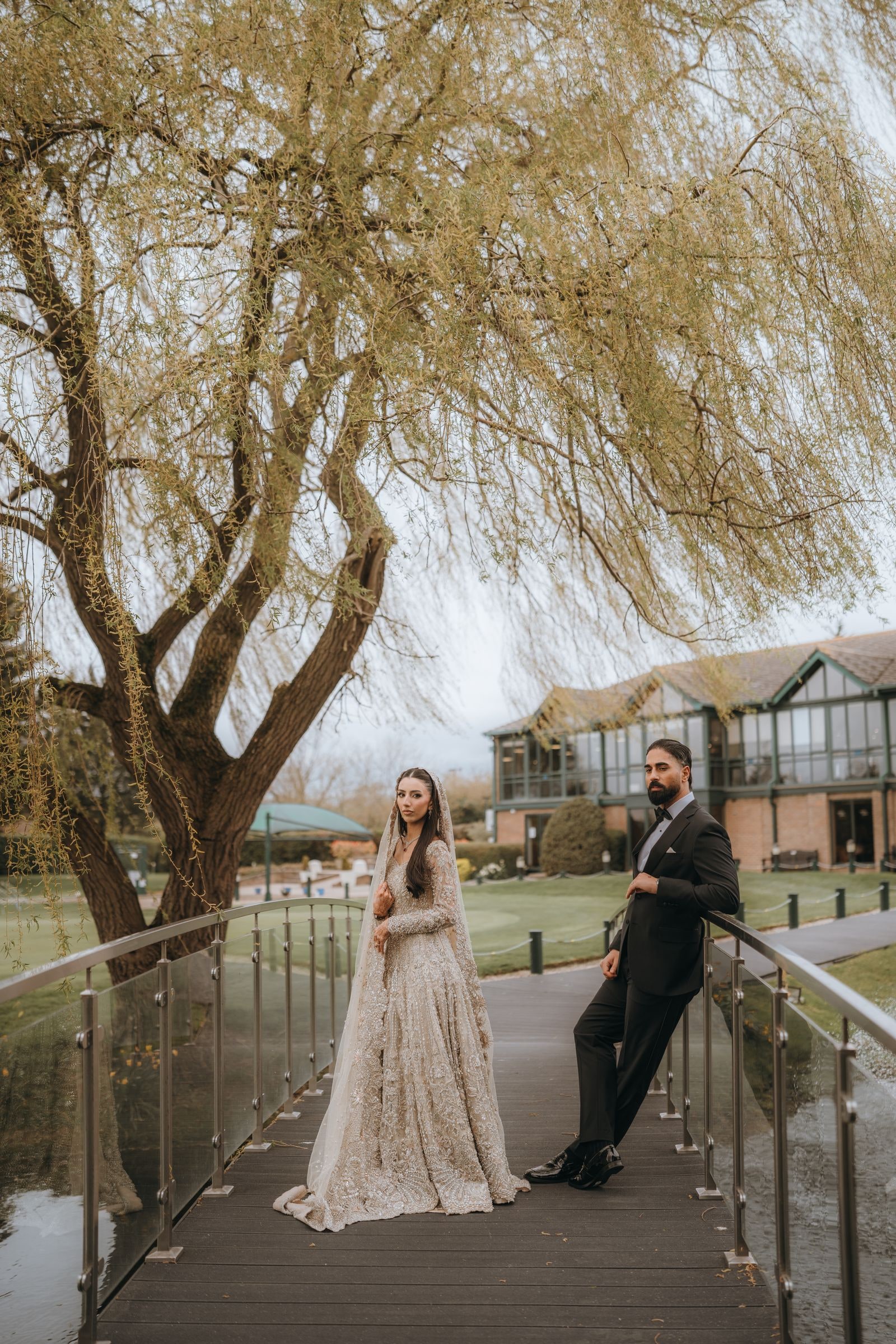 Bride and groom on the footbridge beneath a willow, the clubhouse behind