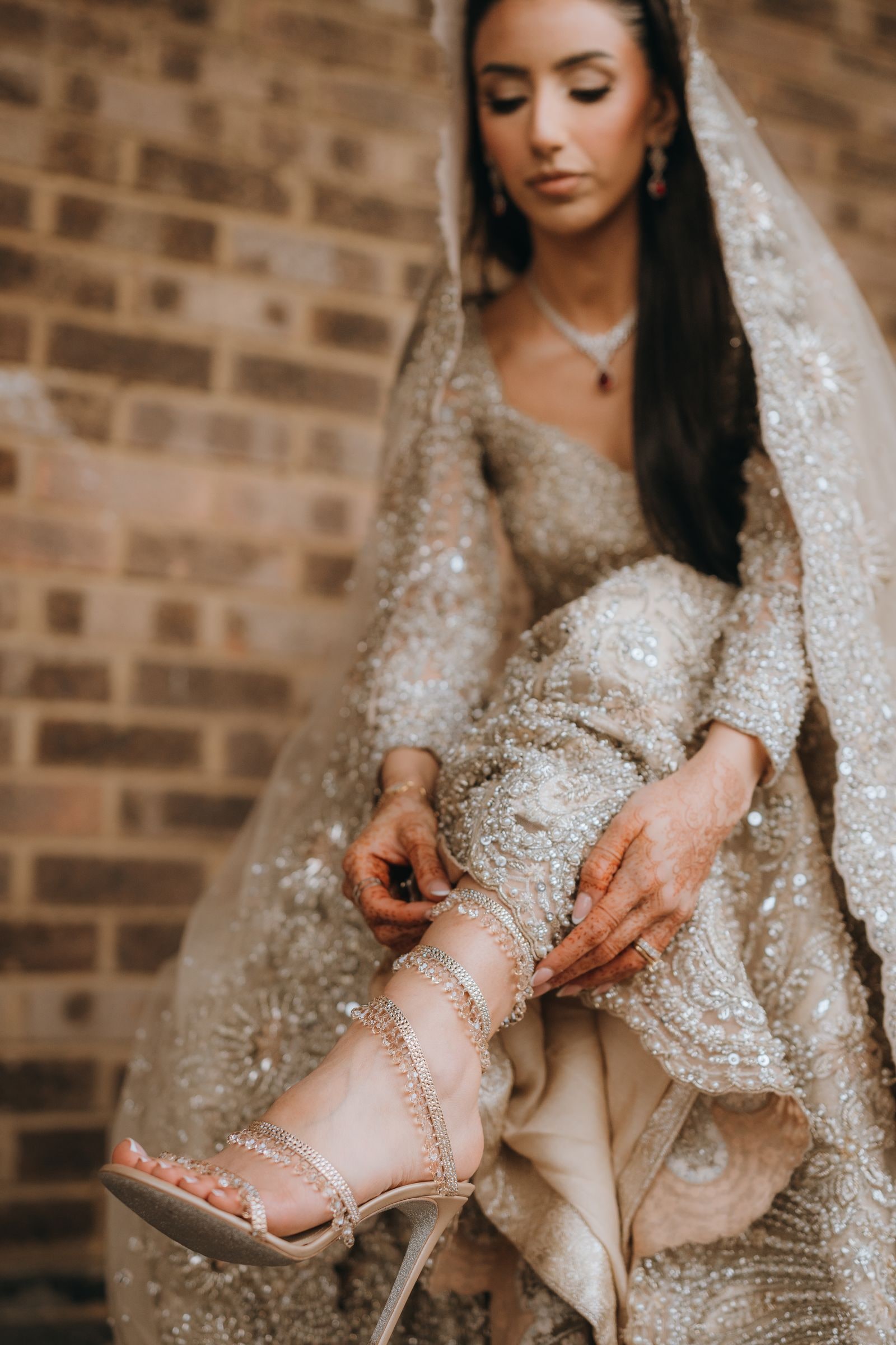 Bride fastening her heeled sandal, her gold embroidered gown gathered up