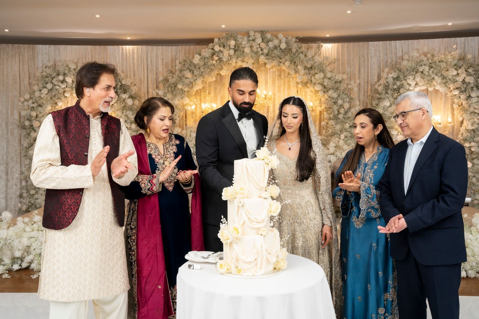 The couple cutting the cake with both families gathered round, applauding
