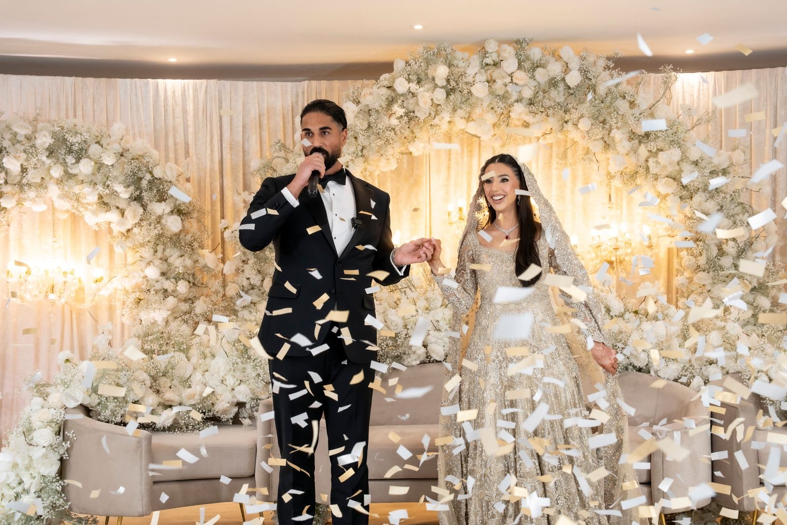 Groom singing into a microphone beside his bride as confetti falls