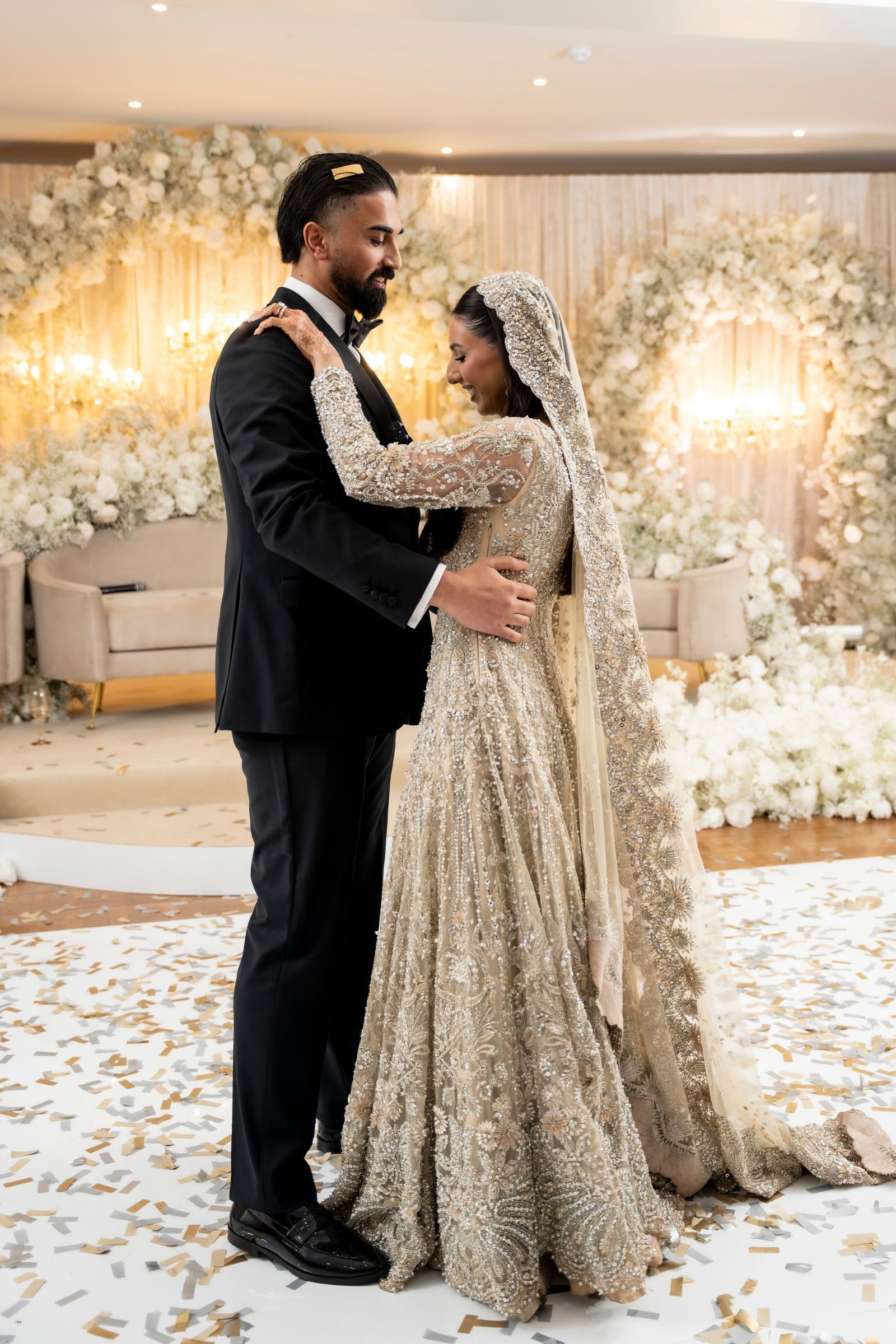 Couple holding each other on the confetti-strewn floor before the flower wall