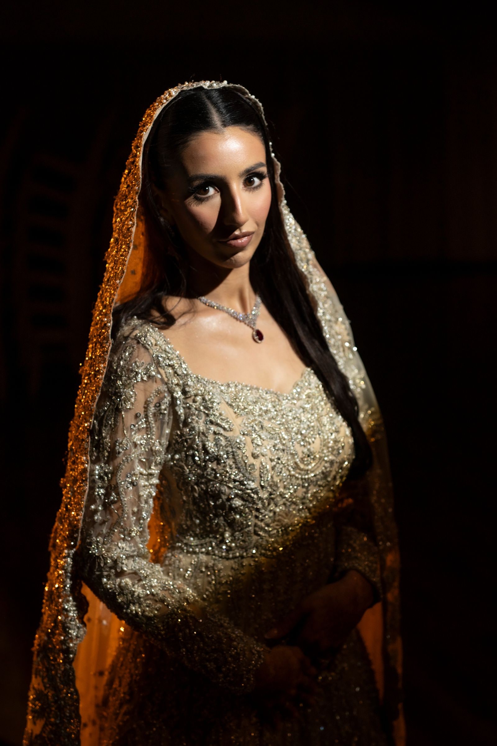 Bride in a gold embroidered gown and veil lit against a dark background