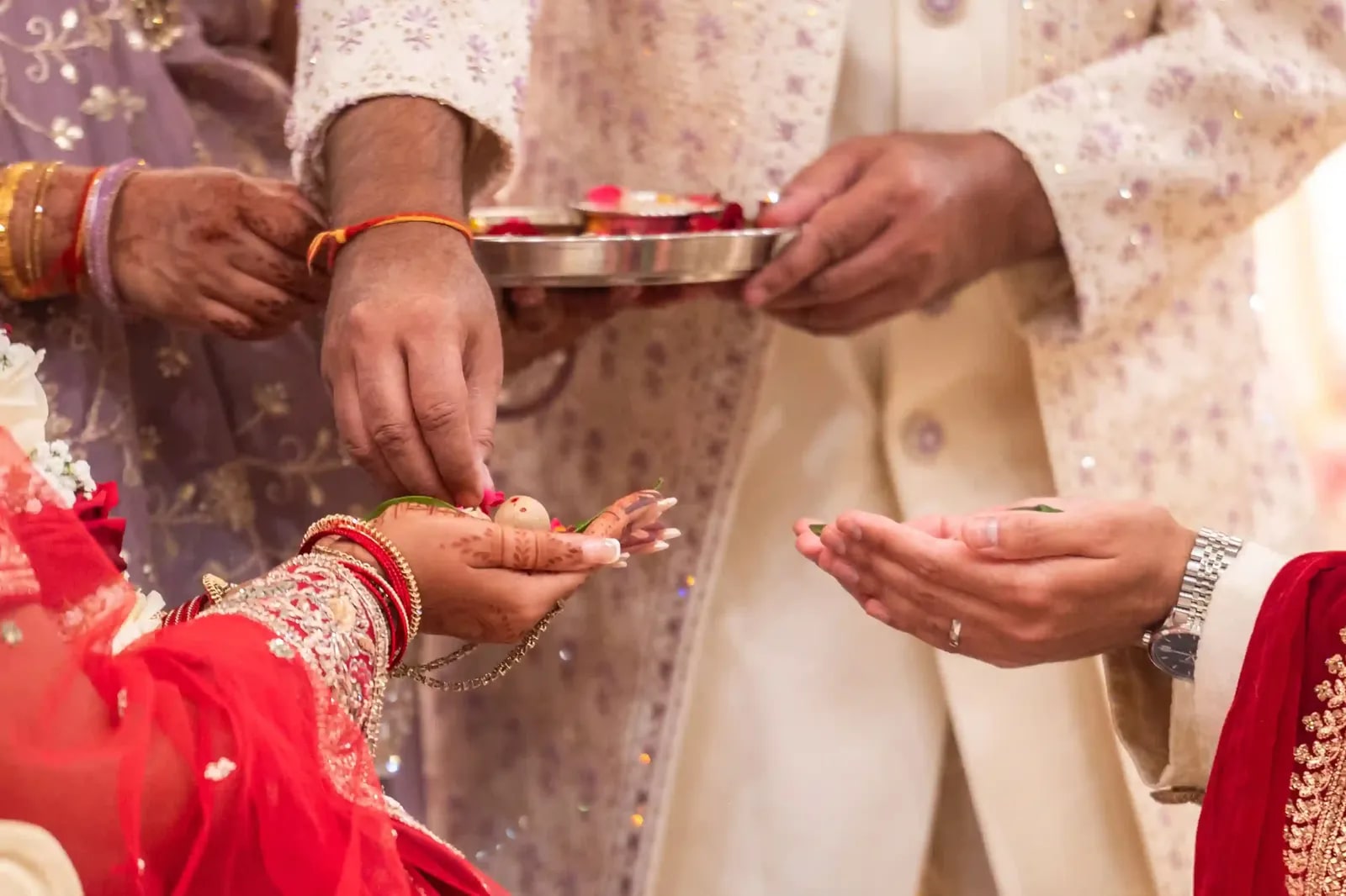 Hands over a small tray of offerings, the bride's wrist heavy with gold