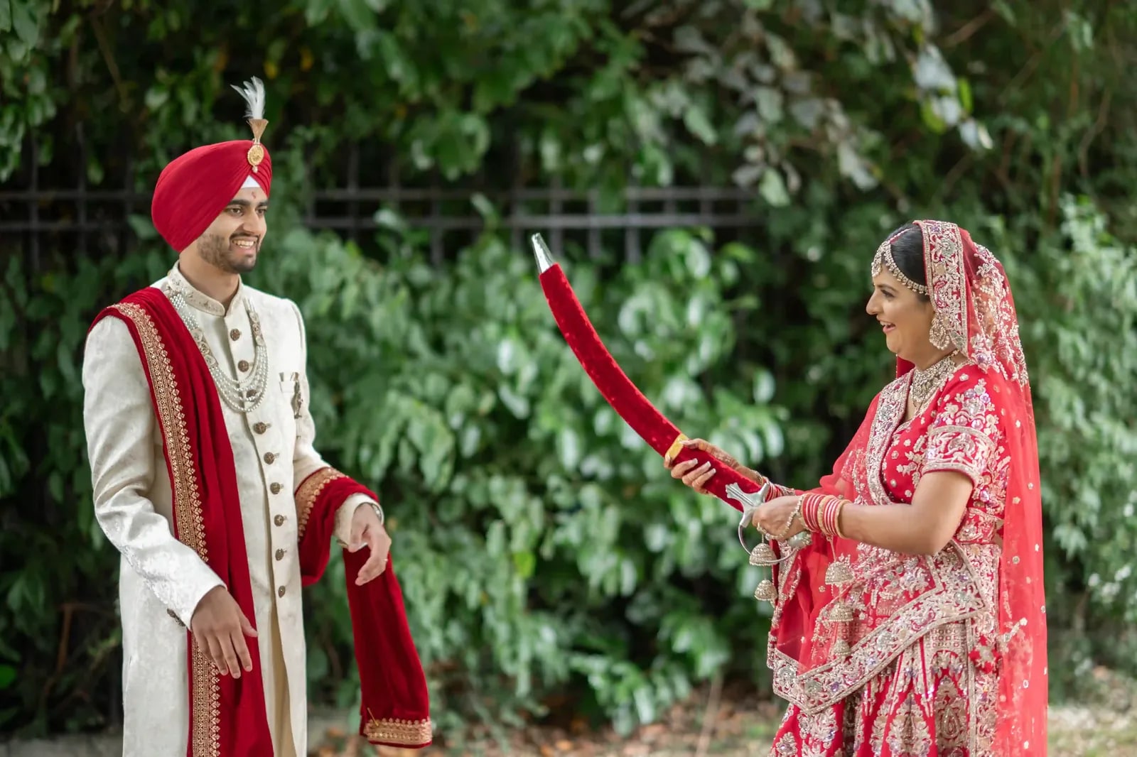 Bride holding the groom's kirpan up between them against a wall of ivy