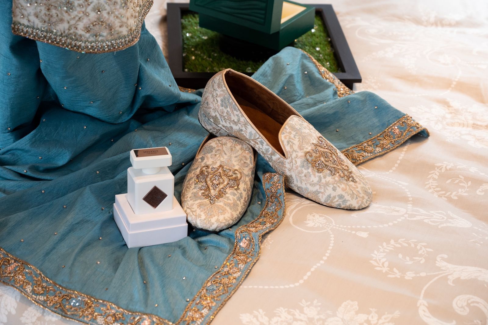 The groom's embroidered shoes and blue shawl laid out with the ring boxes