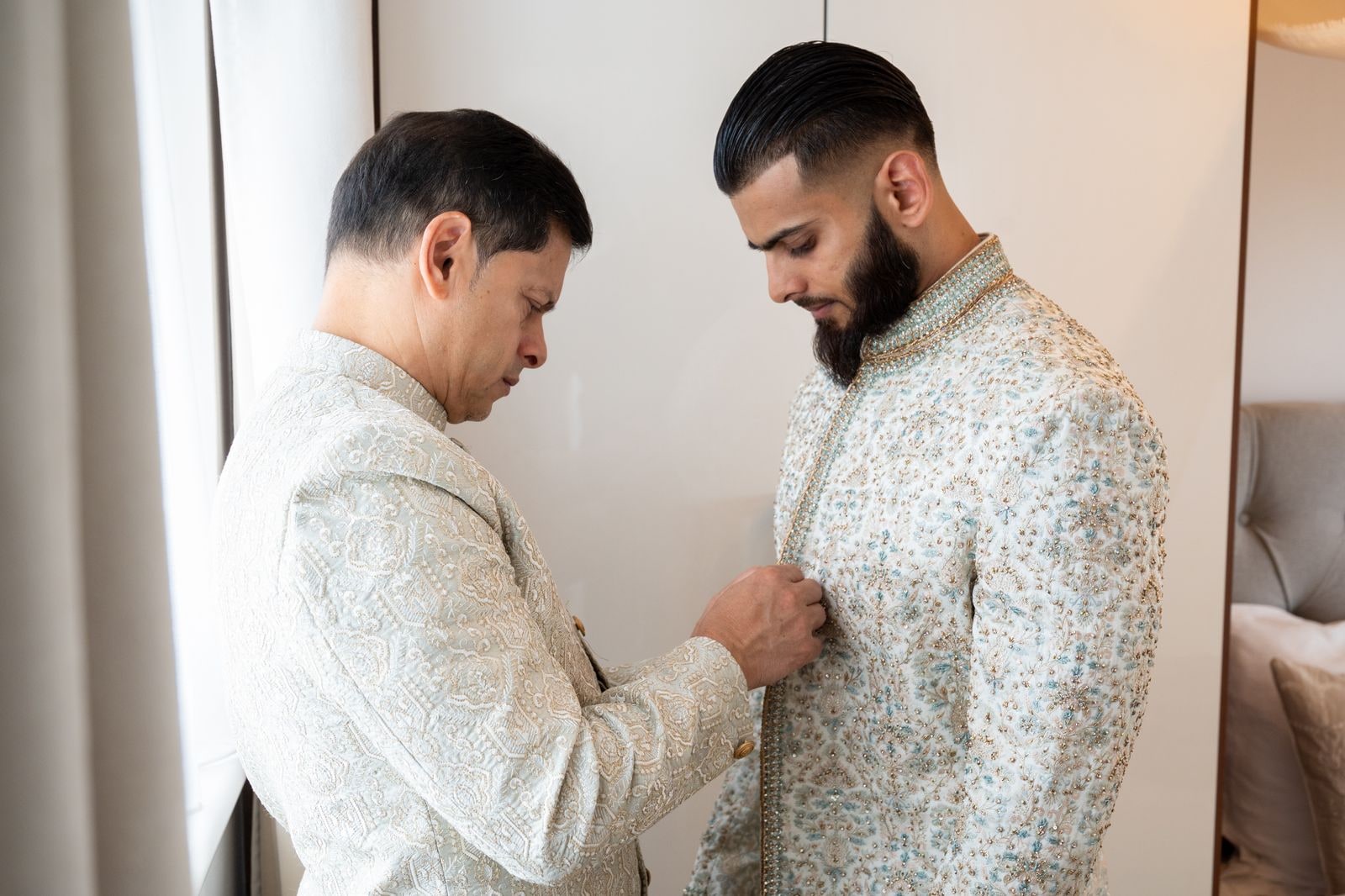The groom's father buttoning his sherwani for him before the ceremony