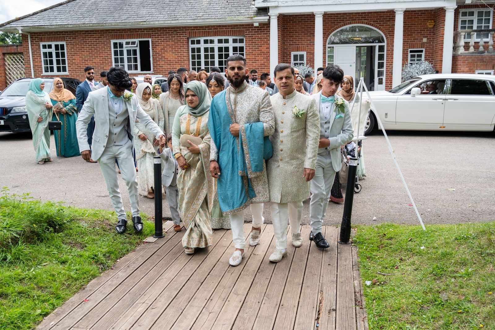 The groom's party walking him in along the boardwalk, a white Rolls-Royce behind