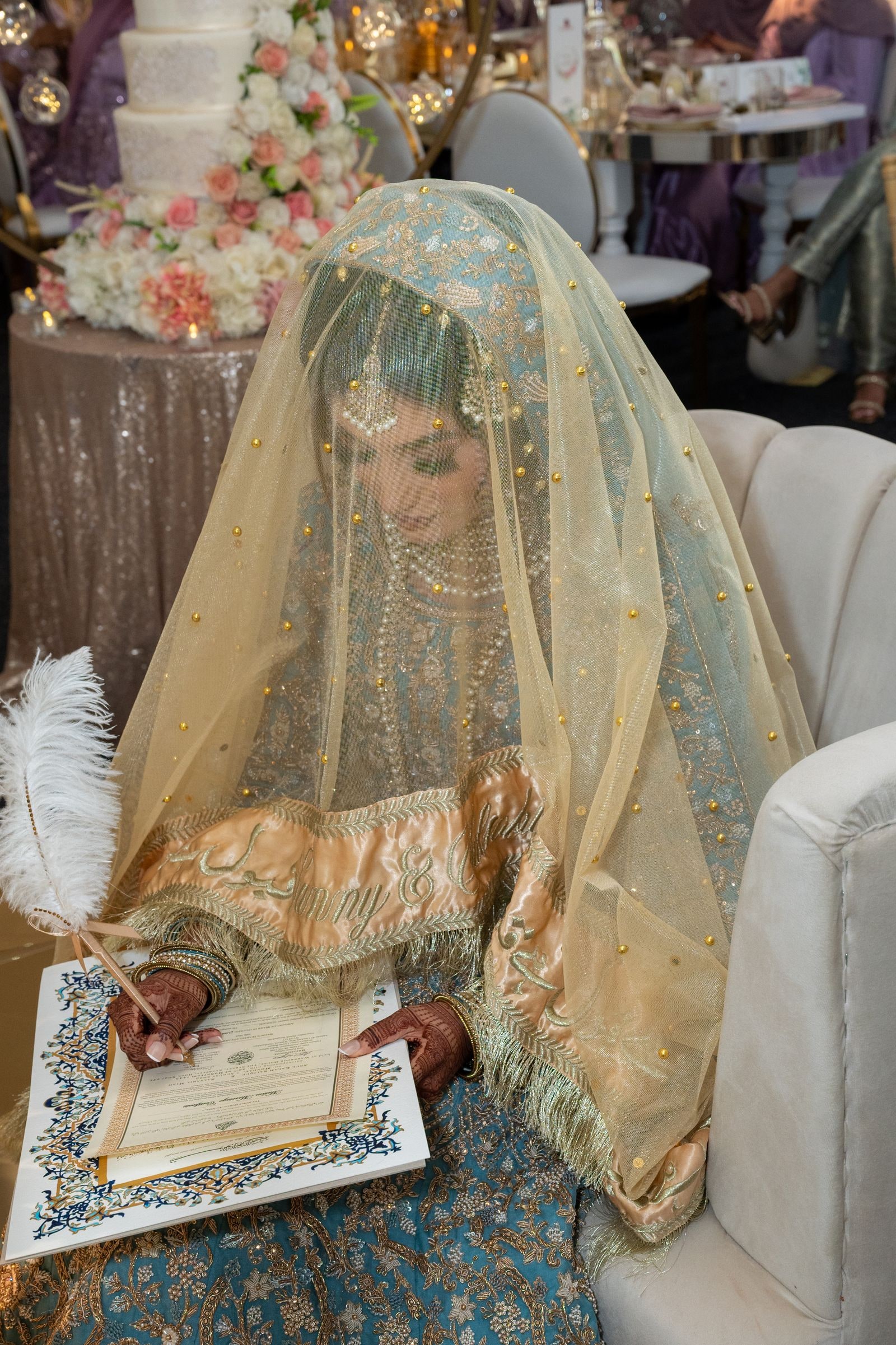 Bride signing the nikkah papers beneath her gold veil