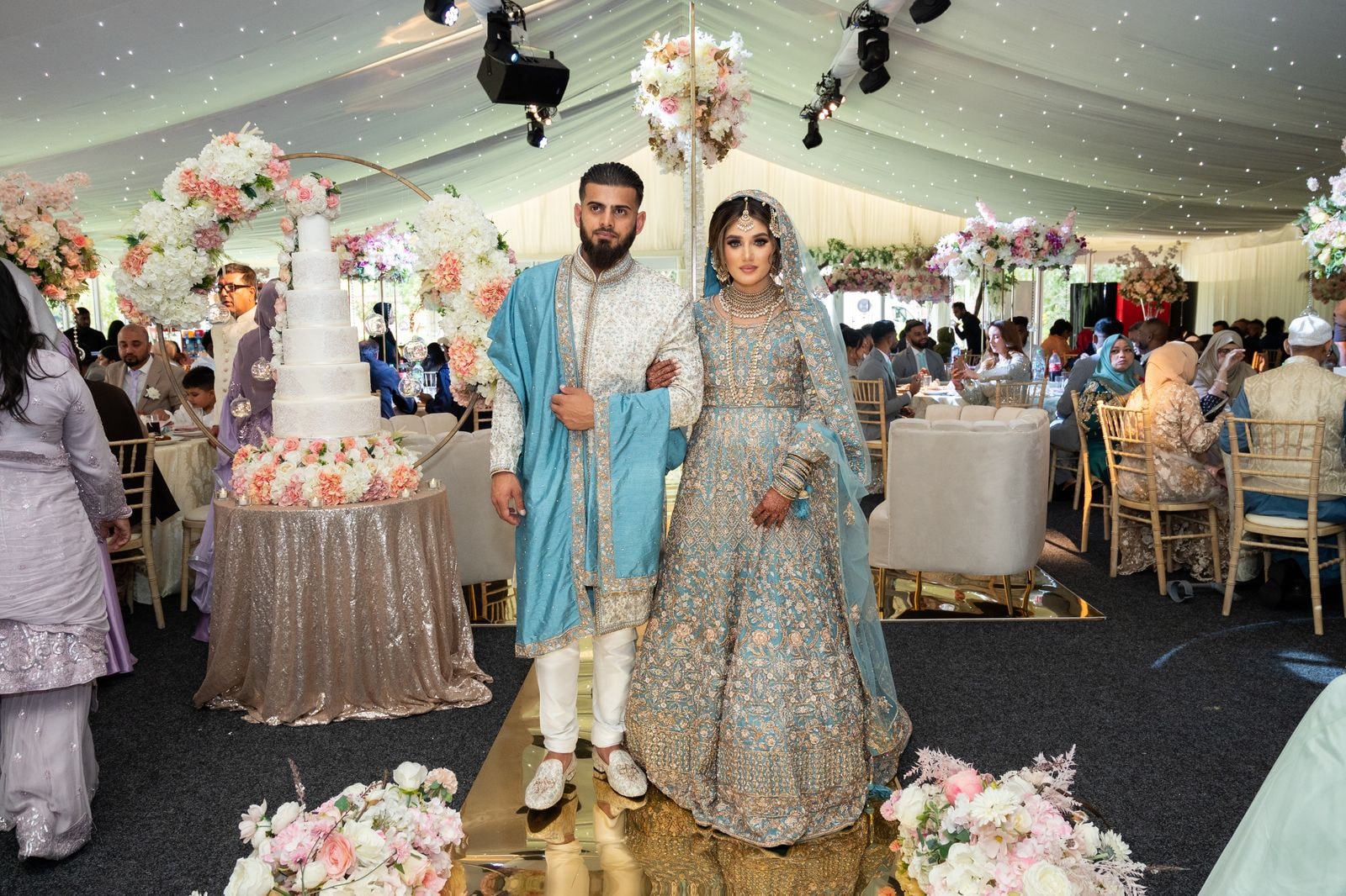Bride and groom walking in past the cake as guests watch from their tables