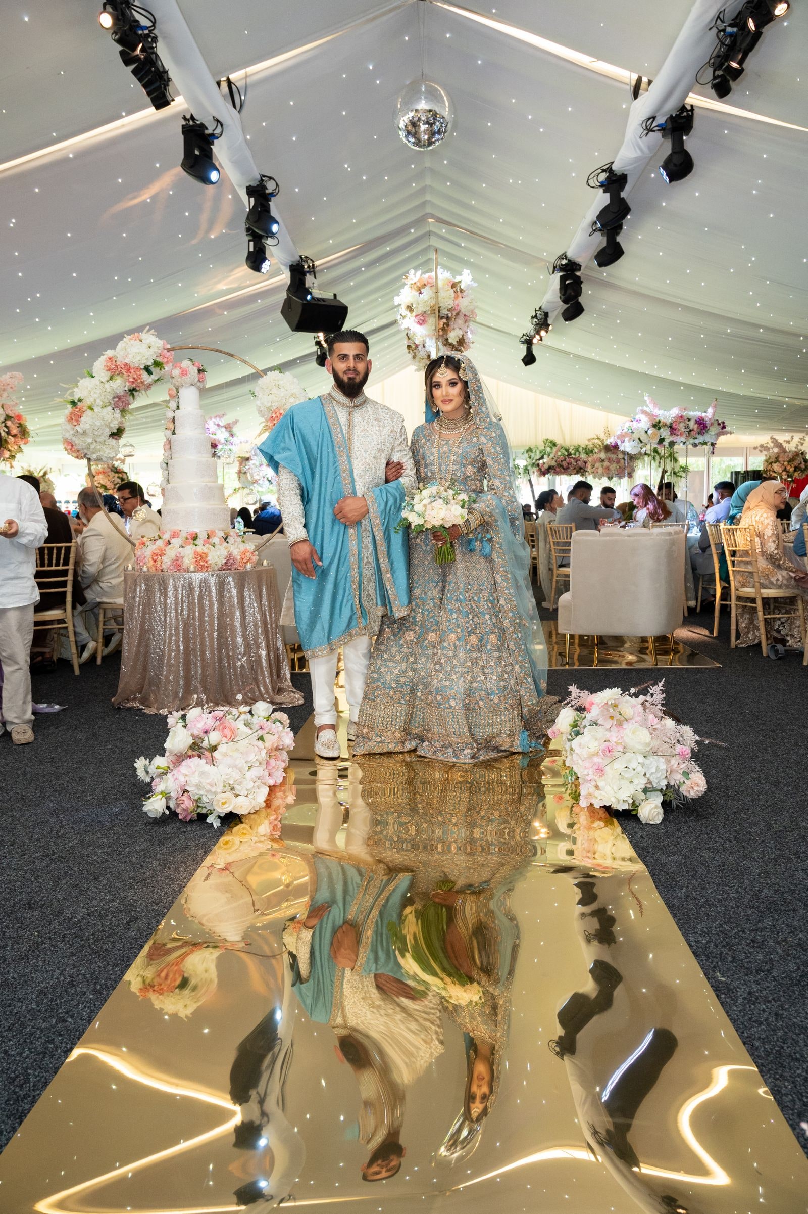 The couple coming down the mirrored gold aisle into the marquee