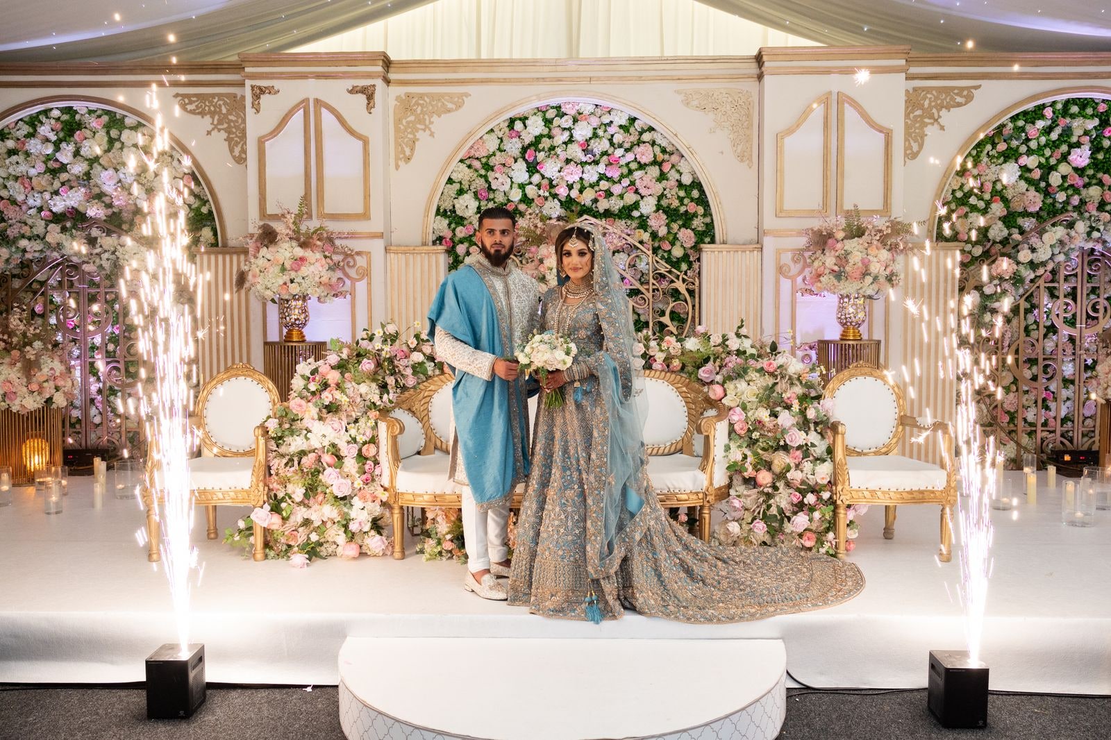 Bride and groom on the flowered stage between two indoor fountains of sparks