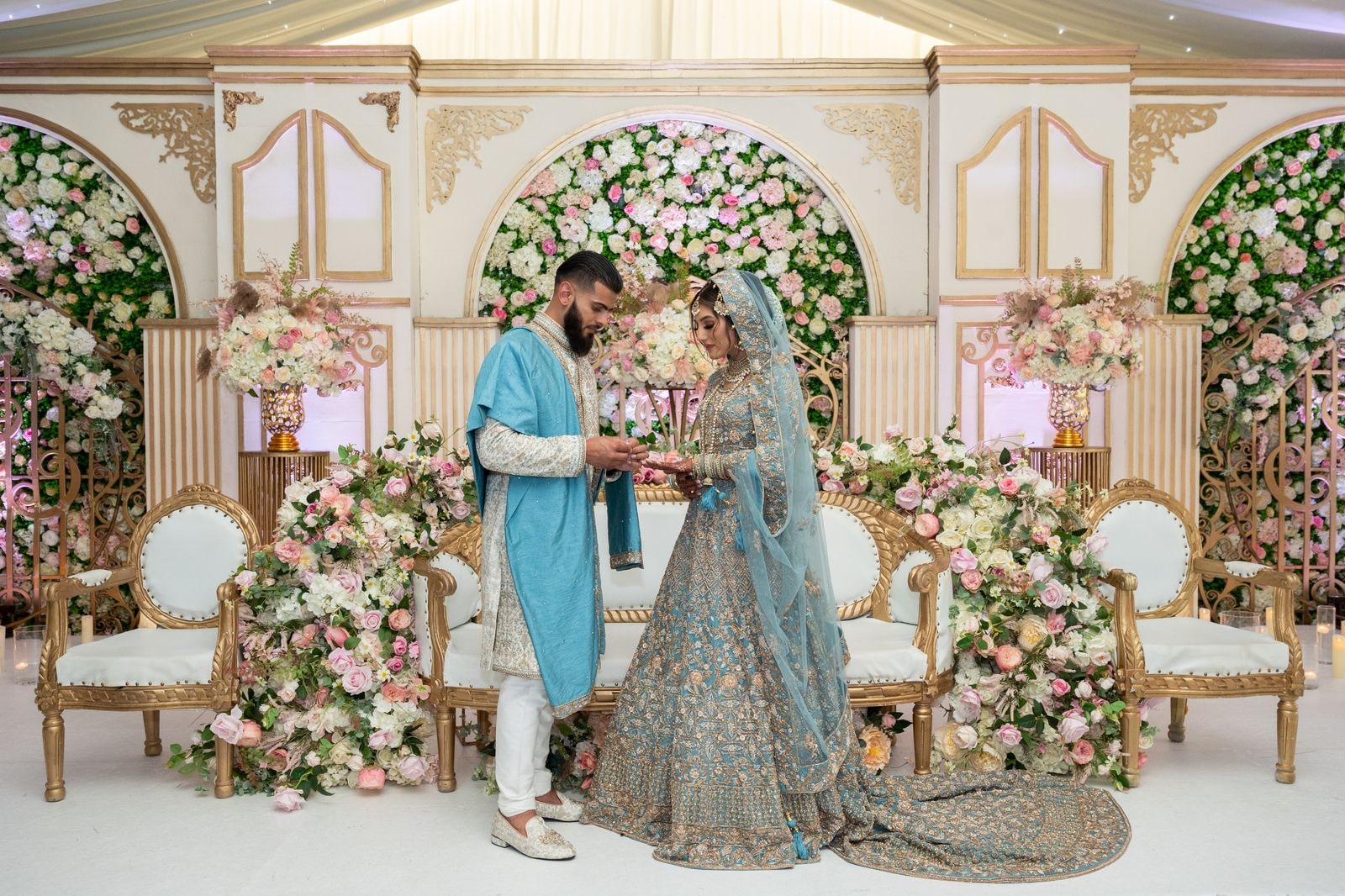 Couple standing together on the flowered stage, her train spread across it