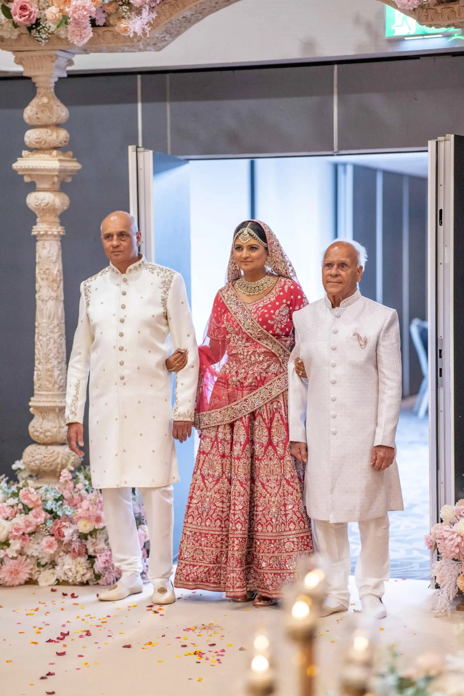 Bride walked in between two men in ivory sherwanis, petals scattered on the floor
