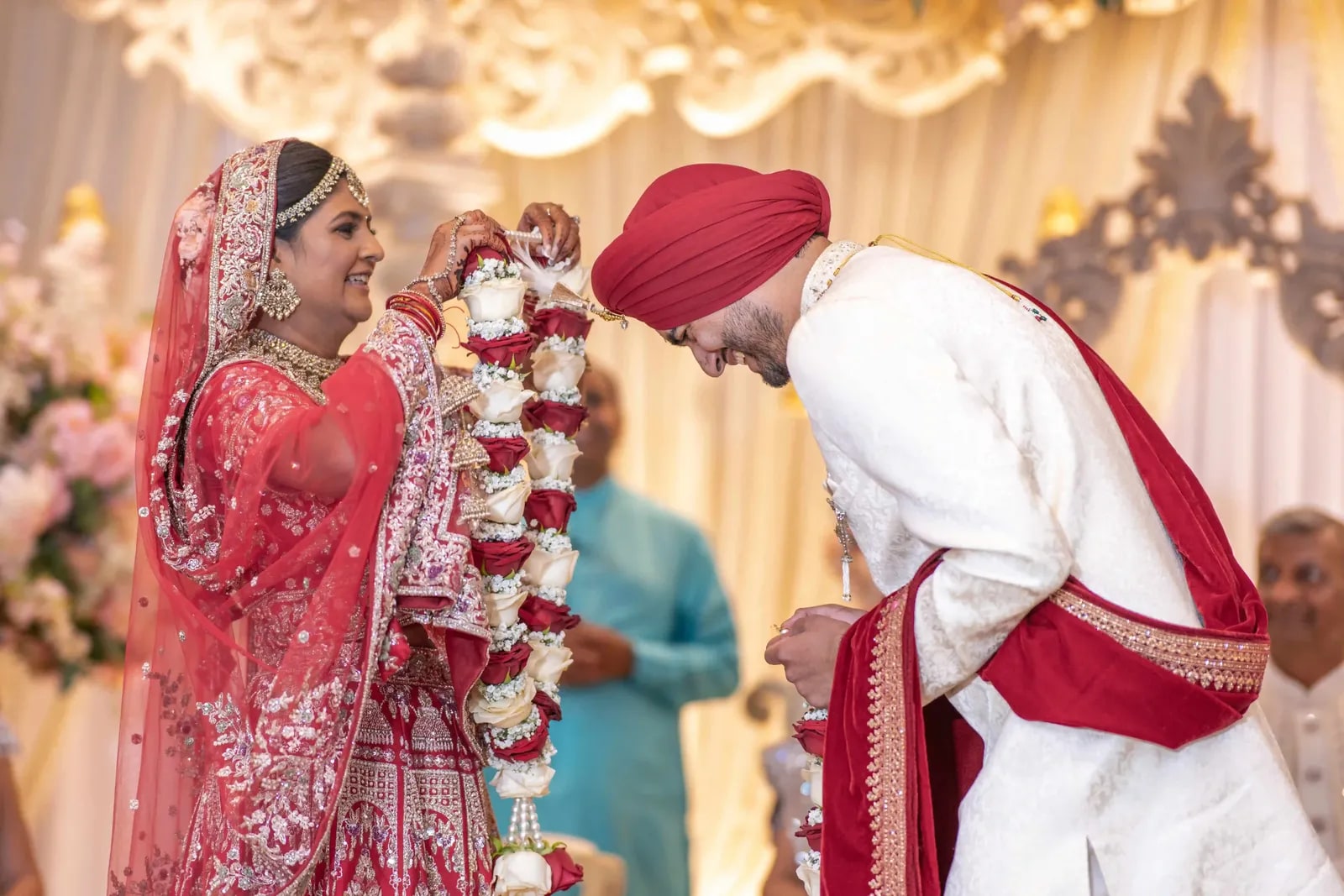 Groom bowing as his bride lifts the garland over his head during the jaimala