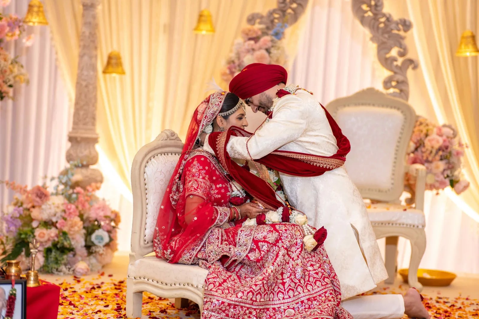 Groom leaning in to his bride where they sit on white and gold chairs