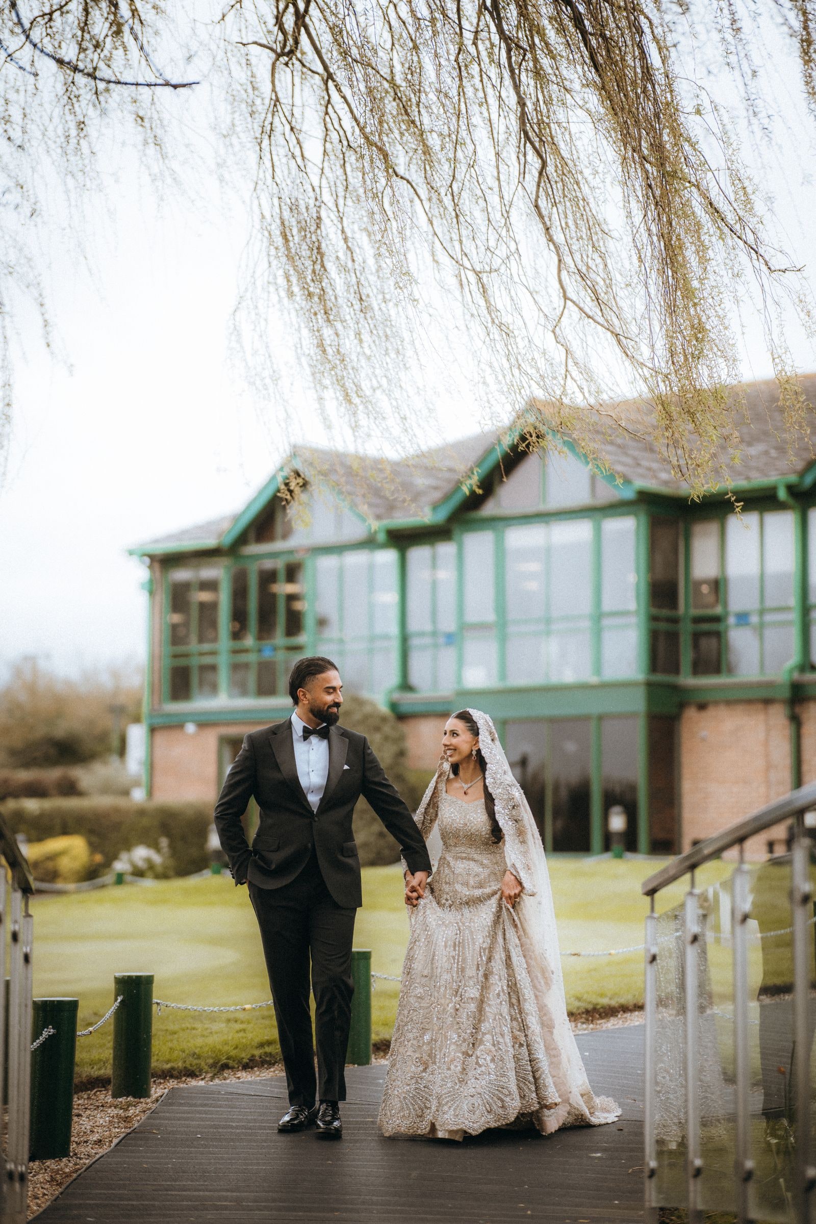 Bride in a pale embroidered gown and groom in black tie walking the boardwalk at Three Rivers