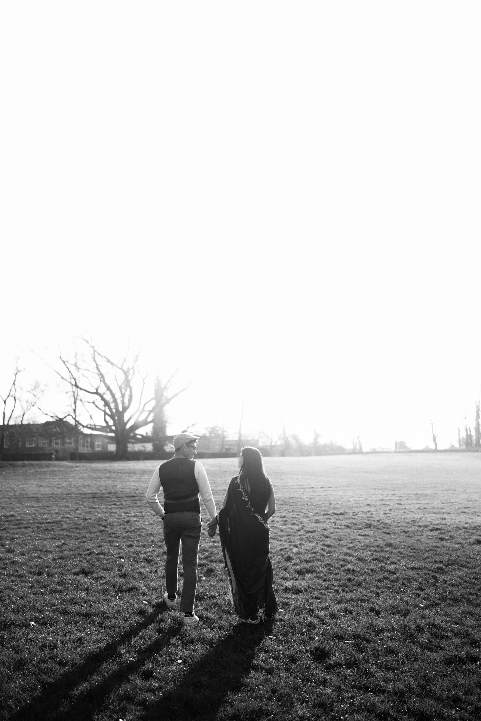 Couple walking away across a frosty field into bright light, in black and white