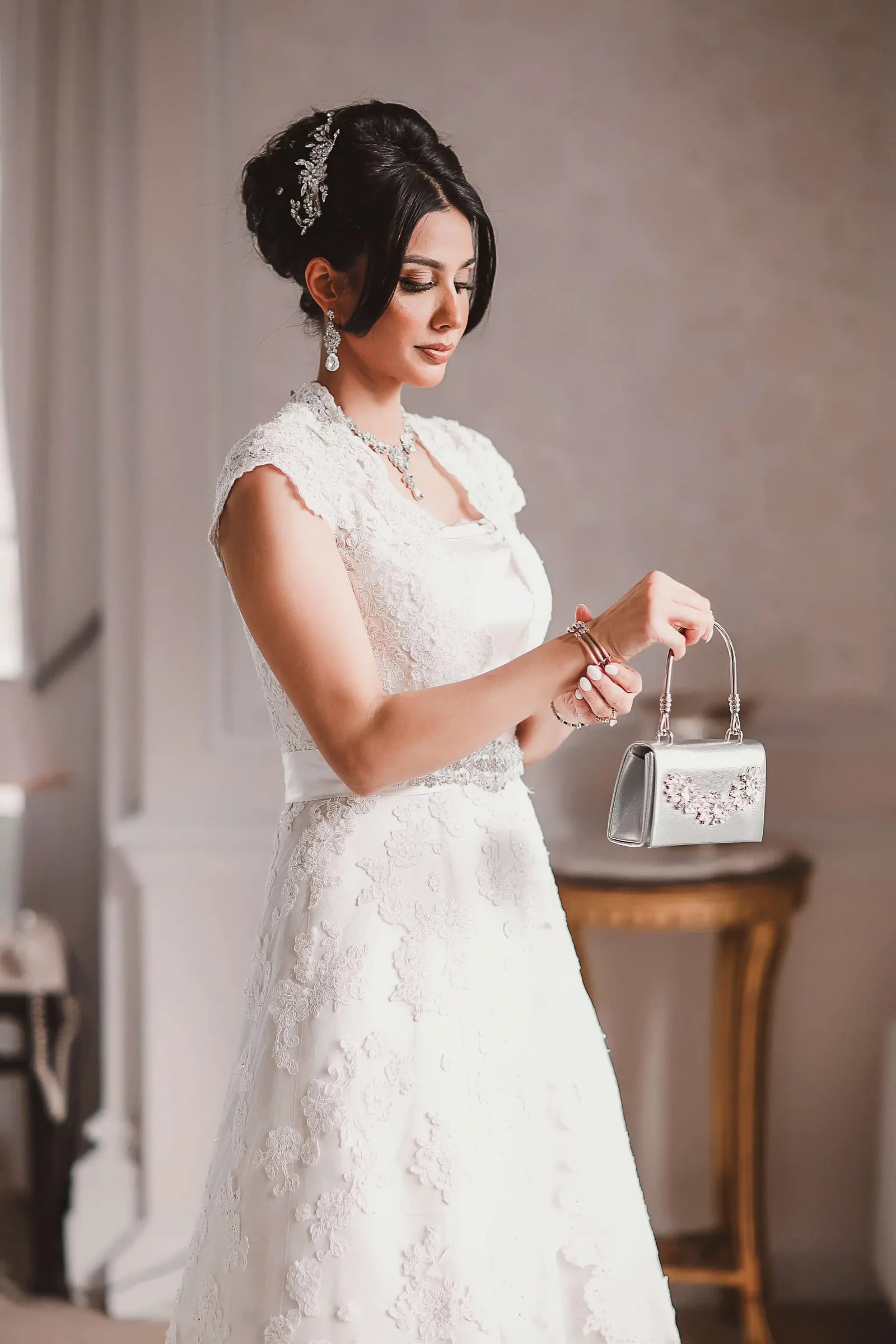 Bride in a lace gown picking up a small white handbag from a gilt table