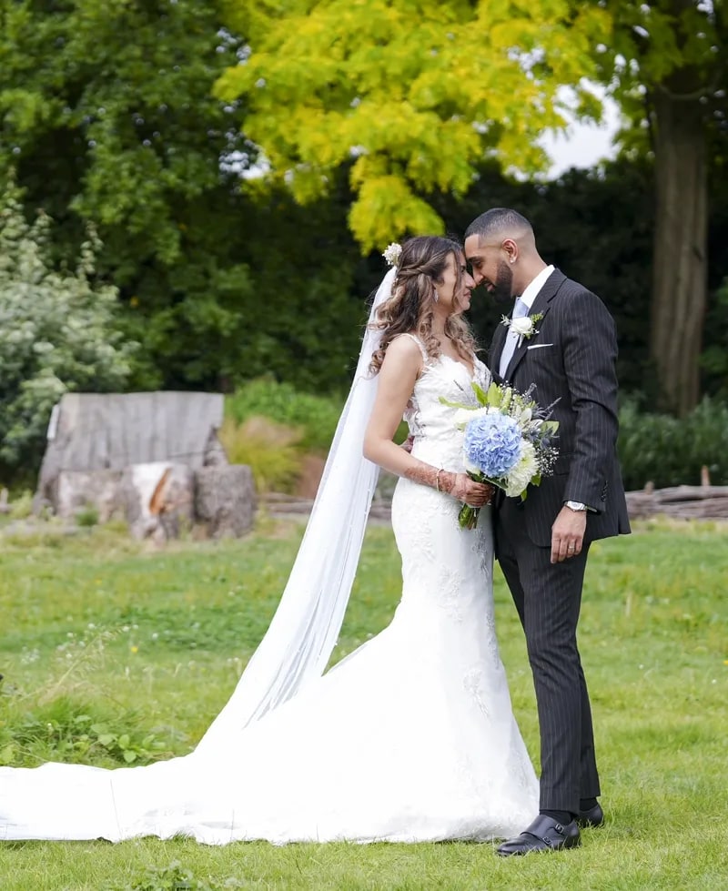 Bride with a blue hydrangea bouquet and groom in black tie under a tree in the churchyard