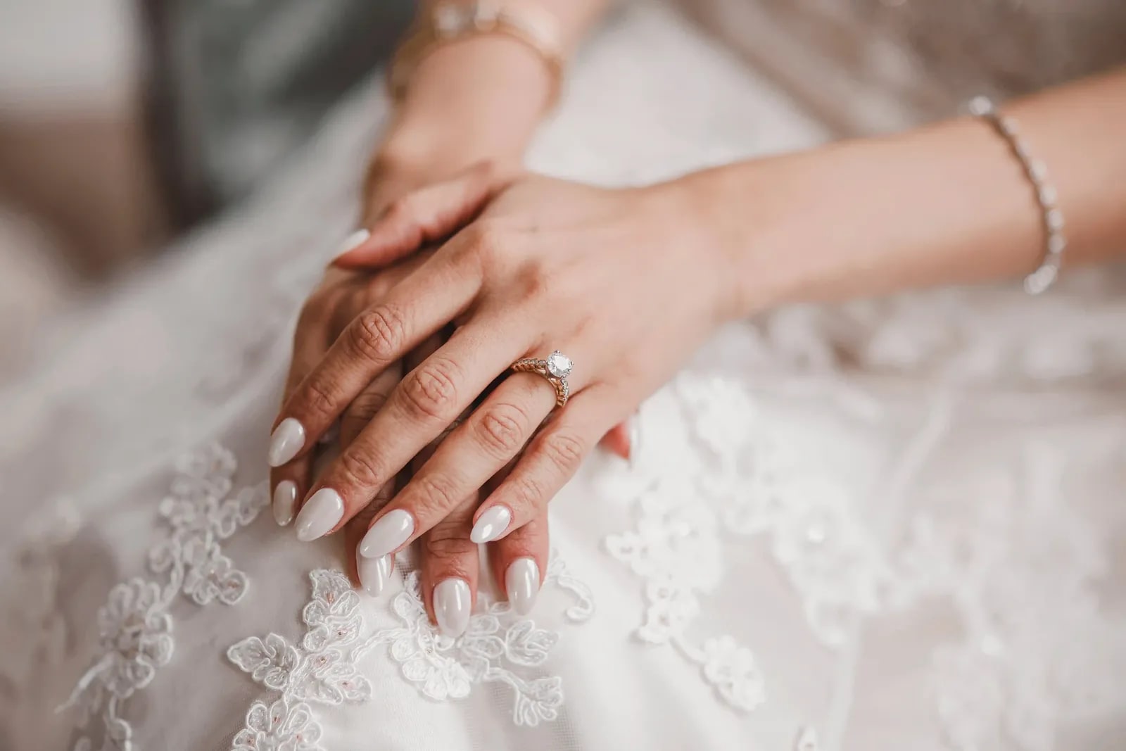 The bride's hands resting on her lace gown, her wedding ring and bracelet in view