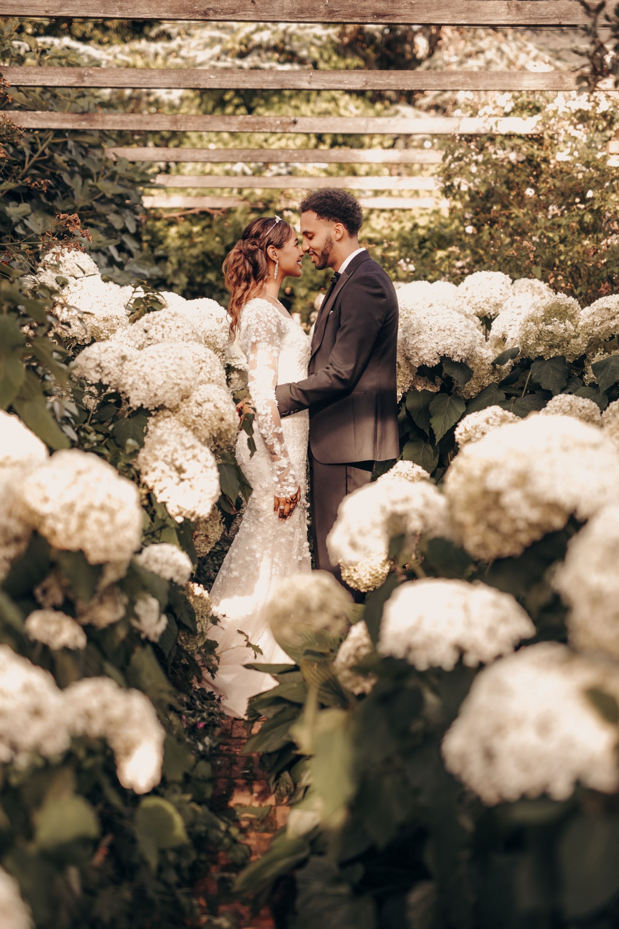 Bride in a long-sleeved lace gown and groom in a three piece suit holding hands on a clipped lawn