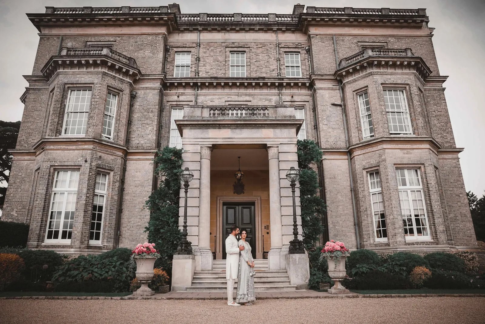 Bride and groom small in the doorway of Hedsor House, the full facade above them