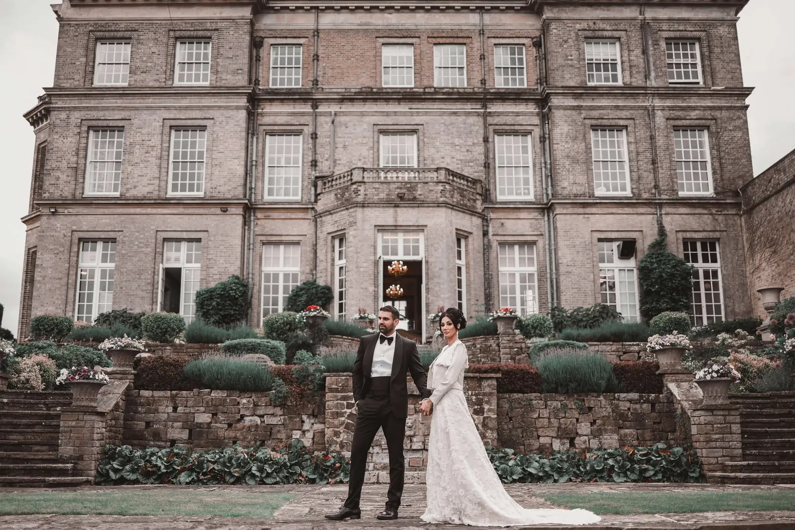 Couple holding hands on the lawn before the stone front of Hedsor House