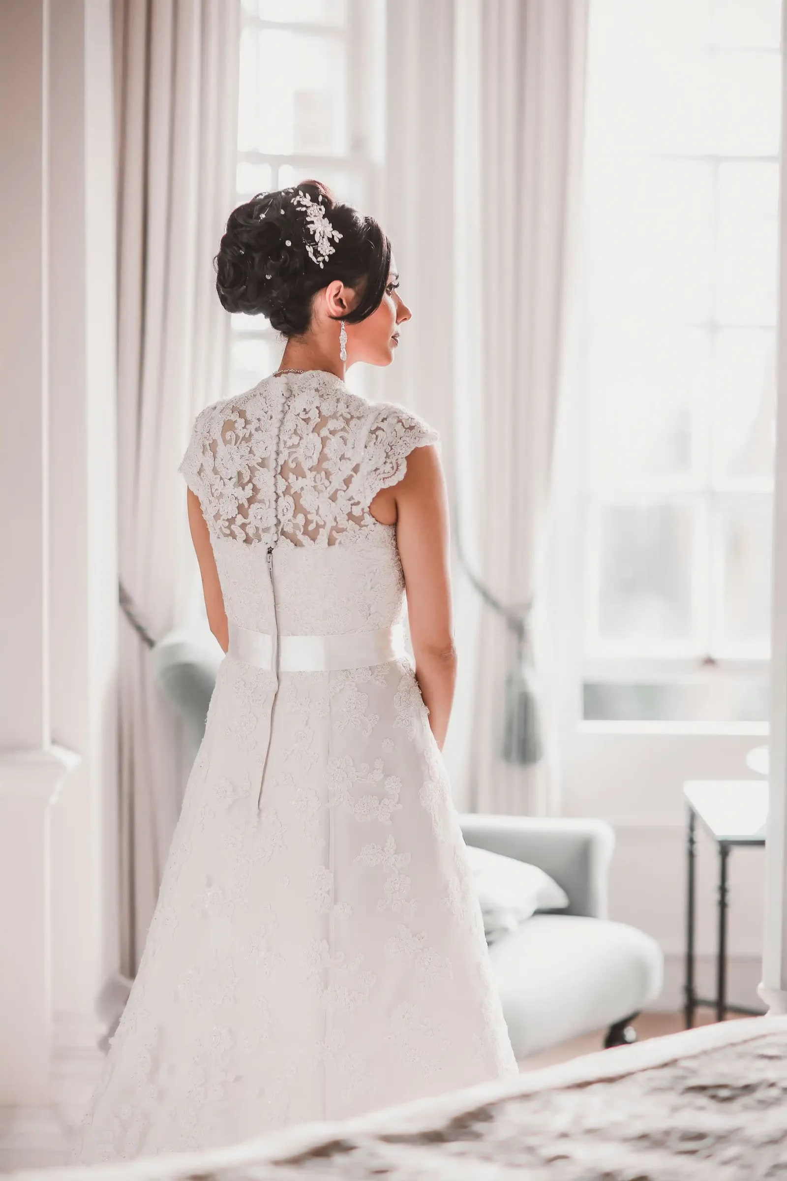 Bride from behind at a window, the lace back of her gown in the light