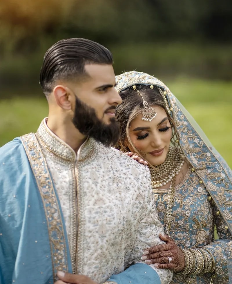 Bride resting against her groom in the garden, her hennaed hand on his arm