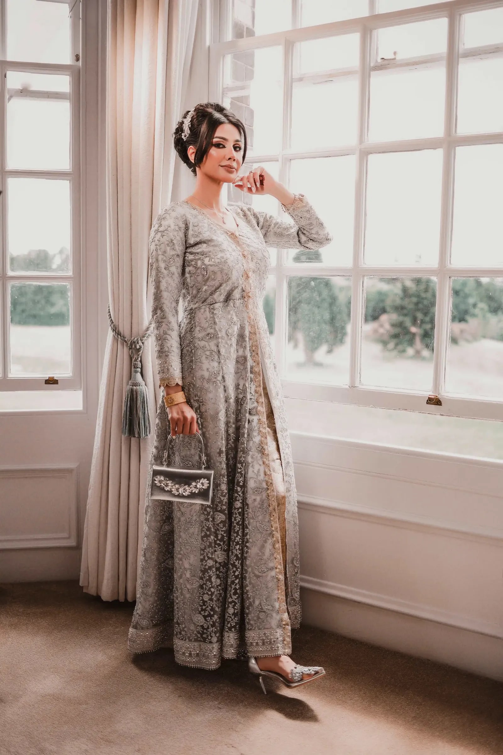 Bride in a silver embroidered gown standing at a tall window