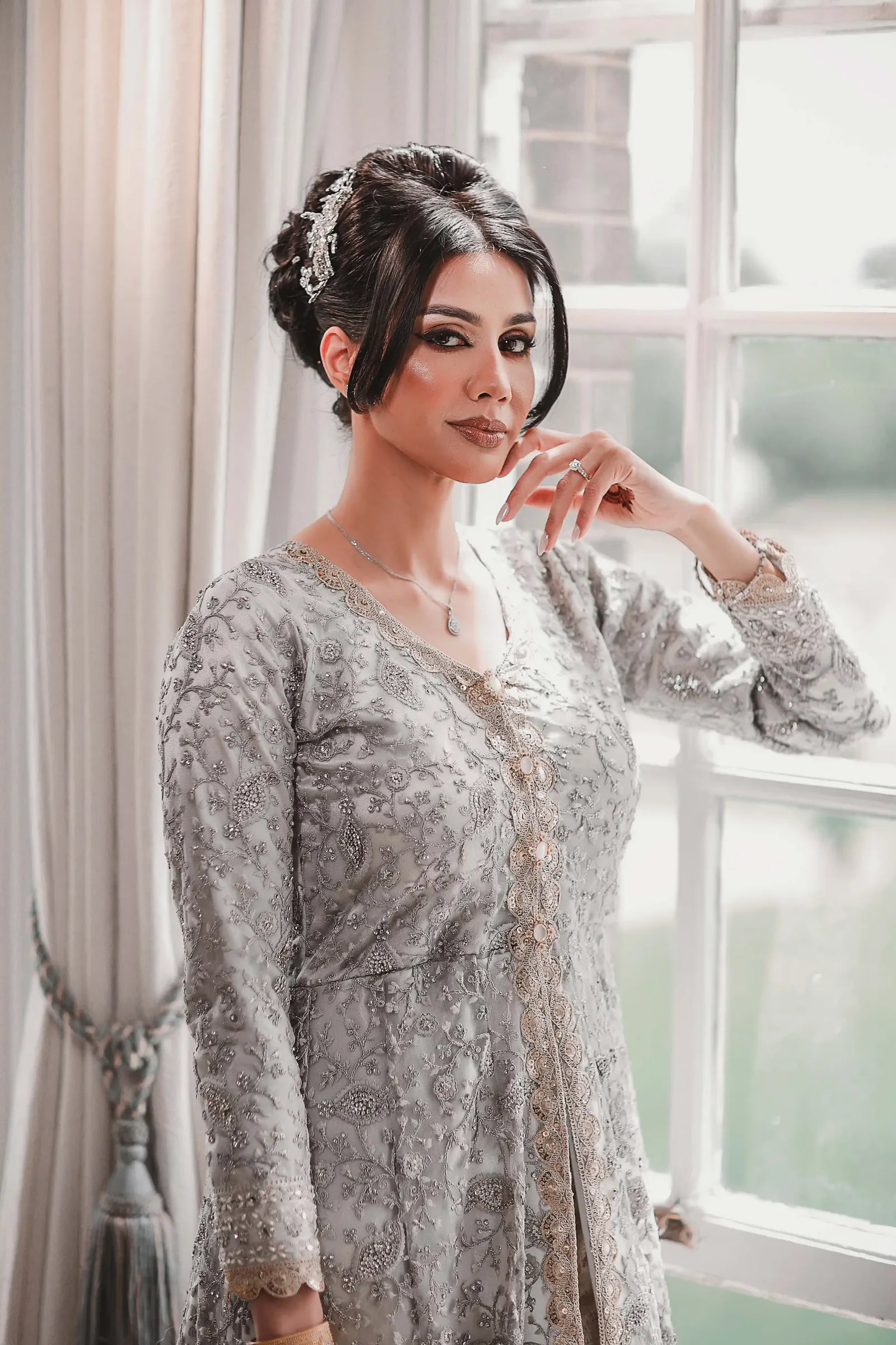 Bride in silver by the window, her hand raised to her chin