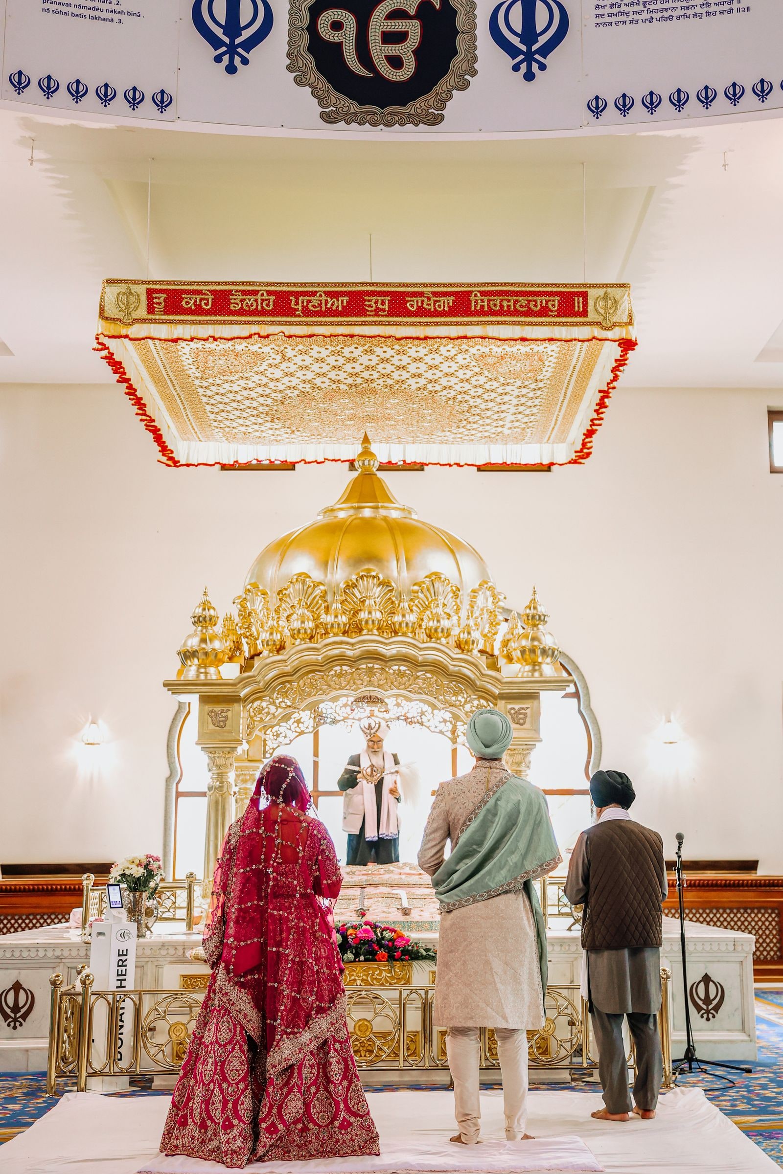 Bride and groom standing before the golden palki in the gurdwara