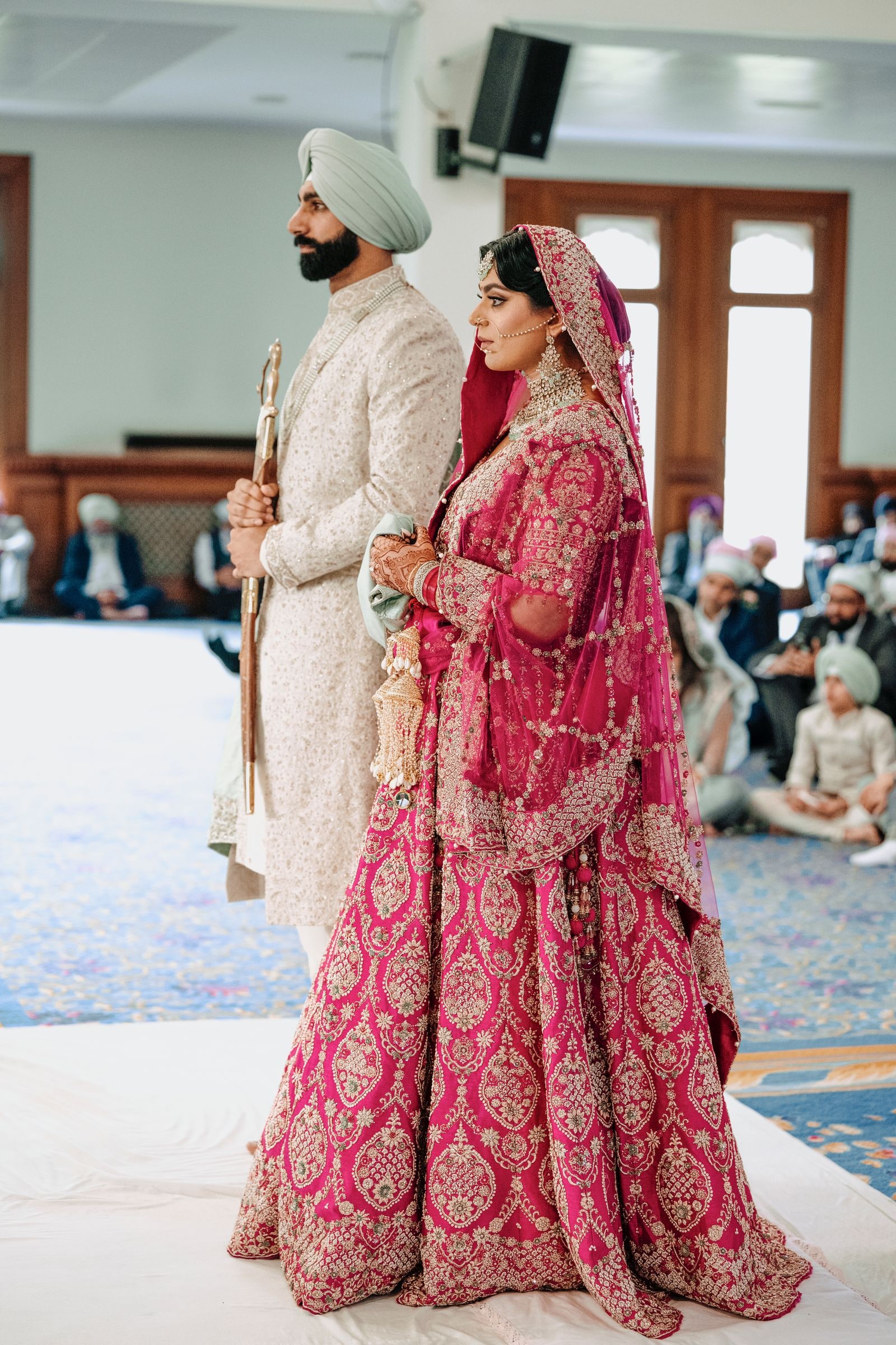 Bride in a deep pink lehenga standing beside her groom in ivory and pale green