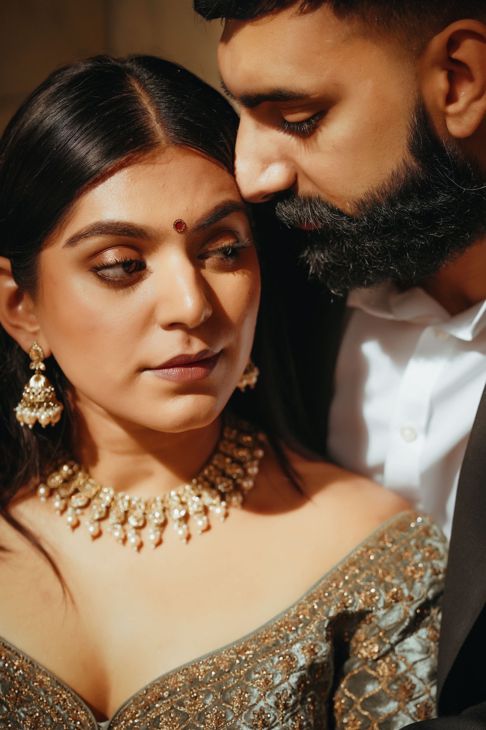 Close portrait of the couple, her gold jhumka earrings and choker against a green lehenga