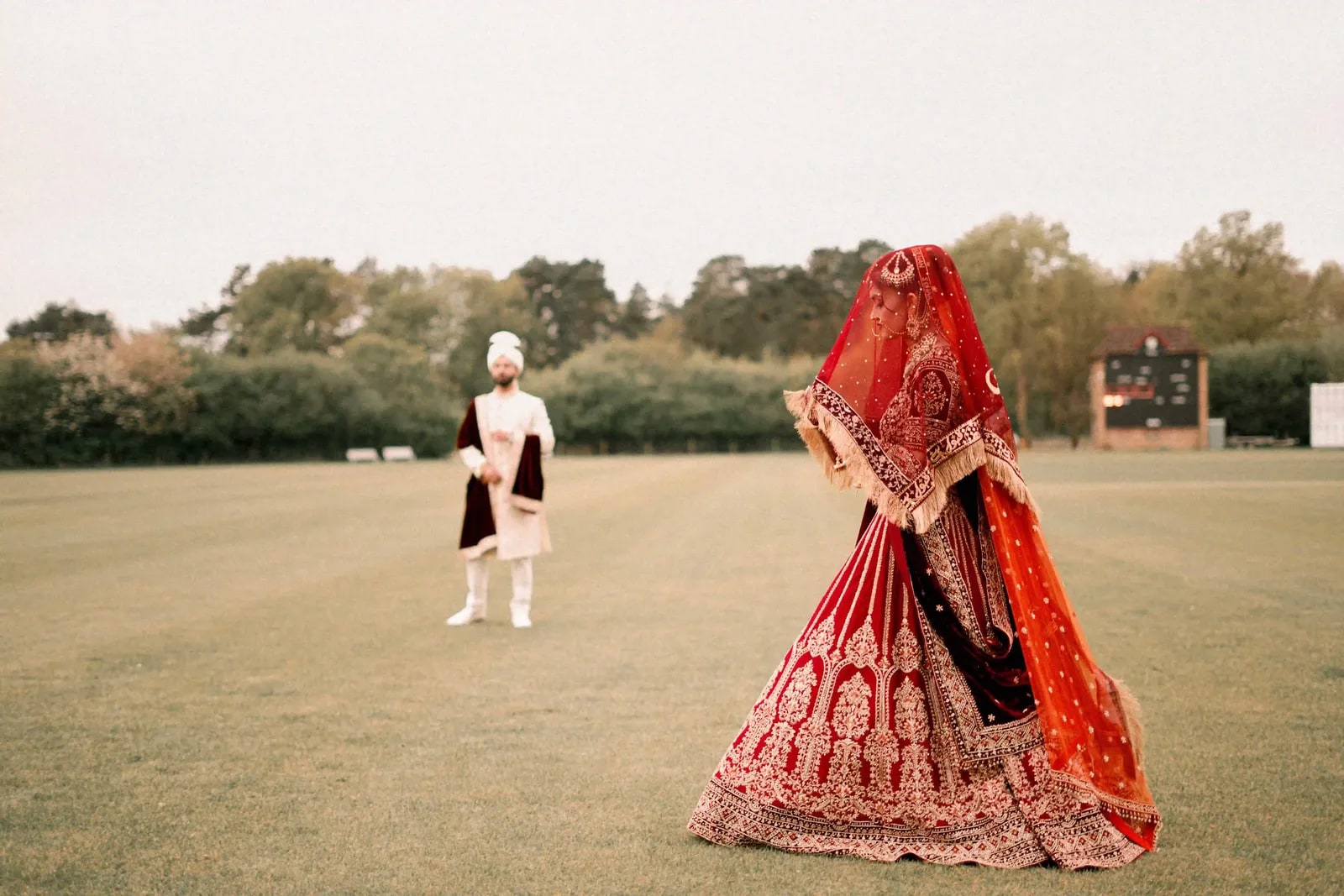 Bride batting on the cricket outfield in her lehenga, her groom bowling at the other end