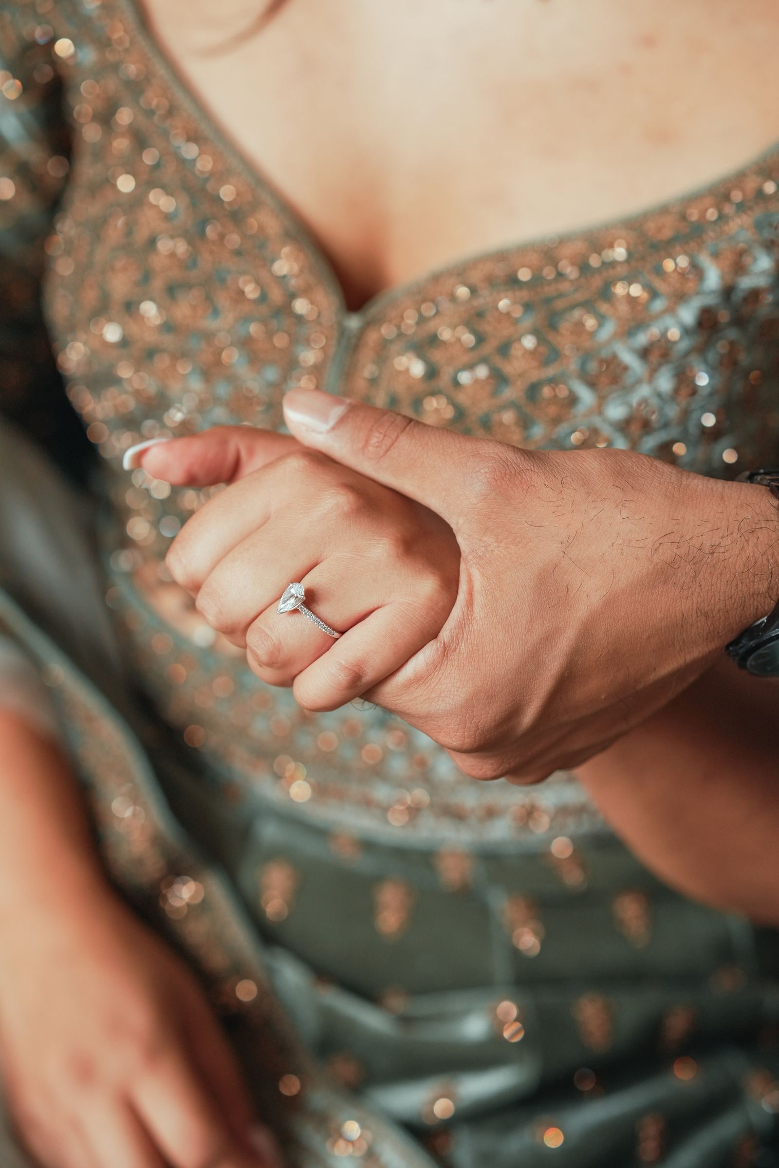 Close view of two hands joined, her engagement ring against her green embroidered dress