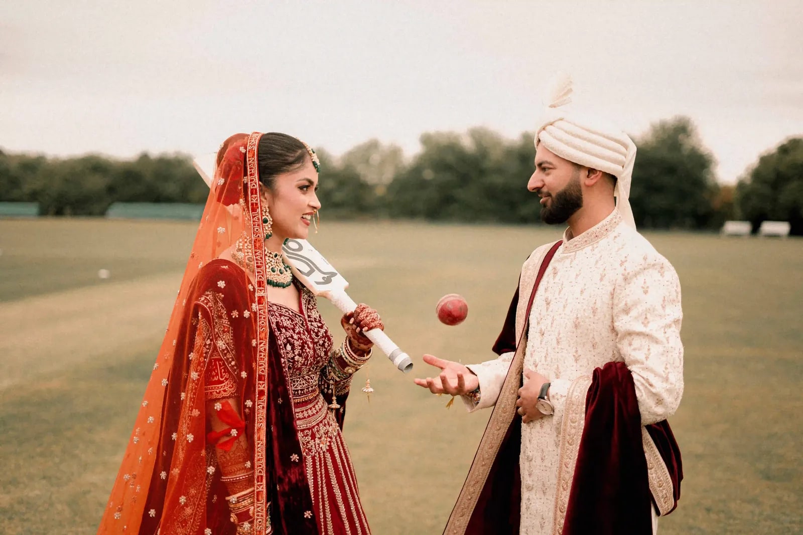 Groom tossing the ball to his bride, who holds the bat in her bangled hands