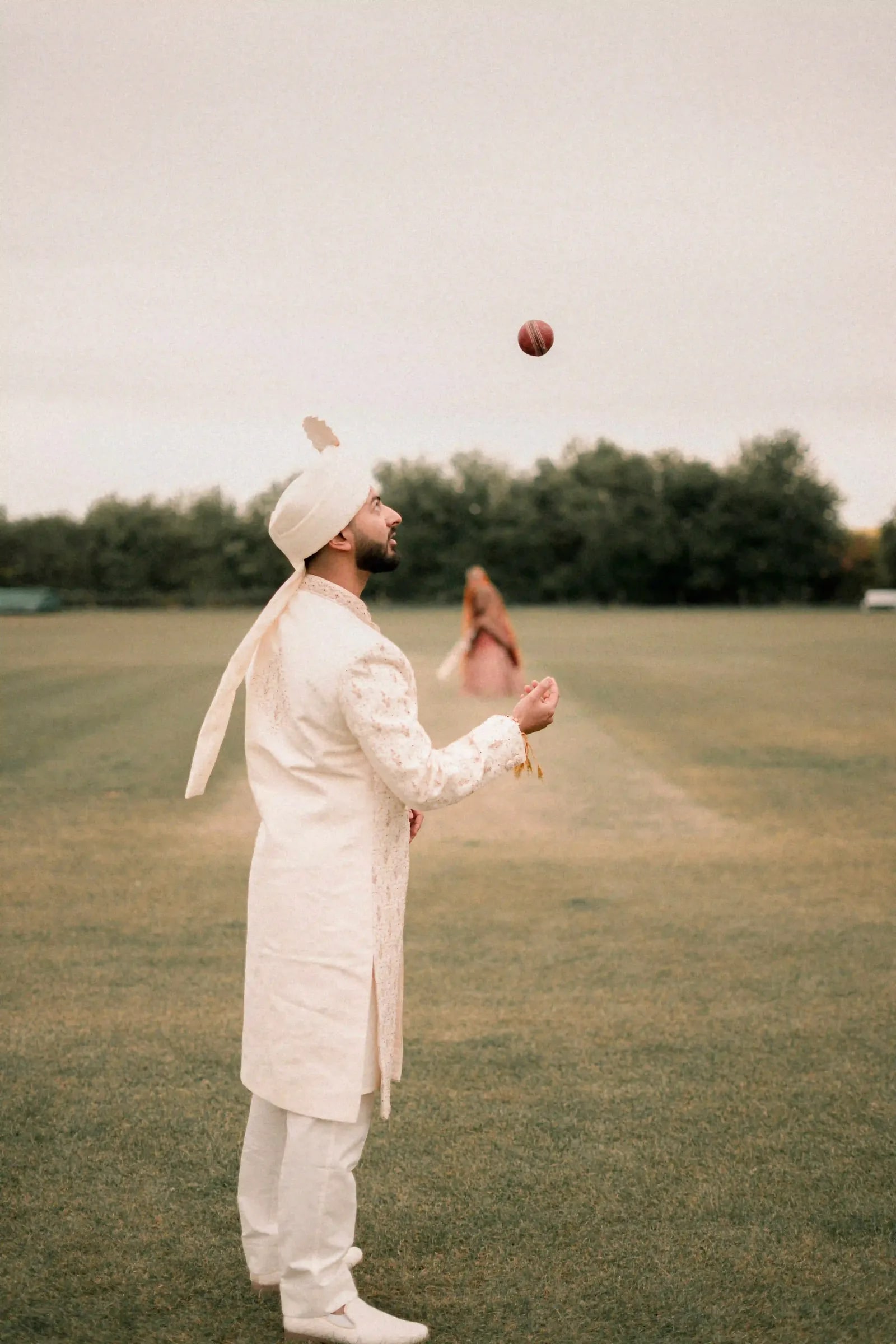 Groom throwing the cricket ball up on the outfield at dusk