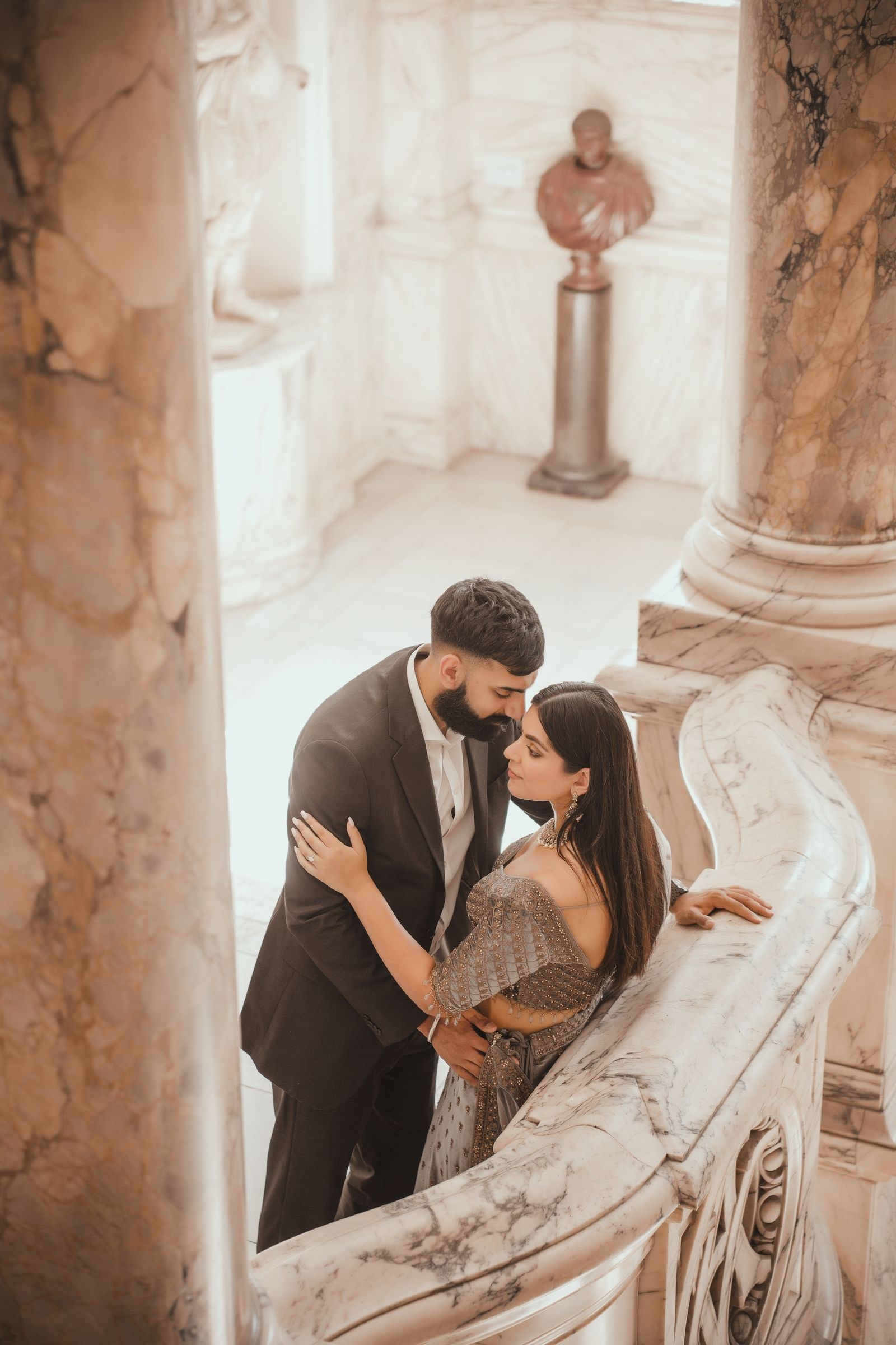Couple holding each other by the marble balustrade beneath a stone bust