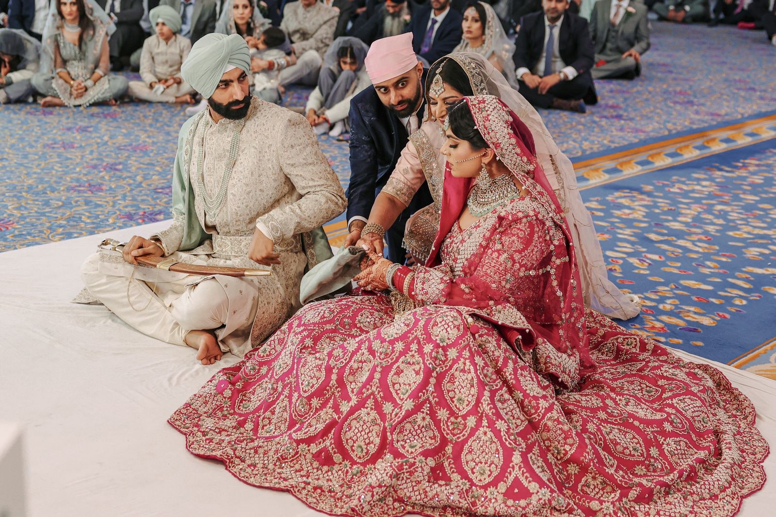 Bride and groom seated on the floor during the ceremony, the congregation behind them