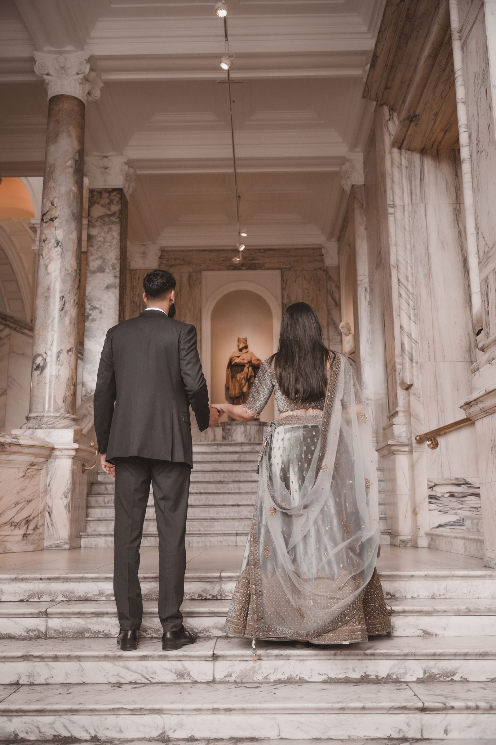 Couple on the stairs from behind, a gilded statue lit in the niche ahead