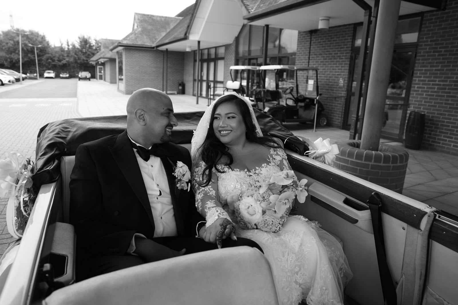 Couple seated in the back of the open car, in black and white