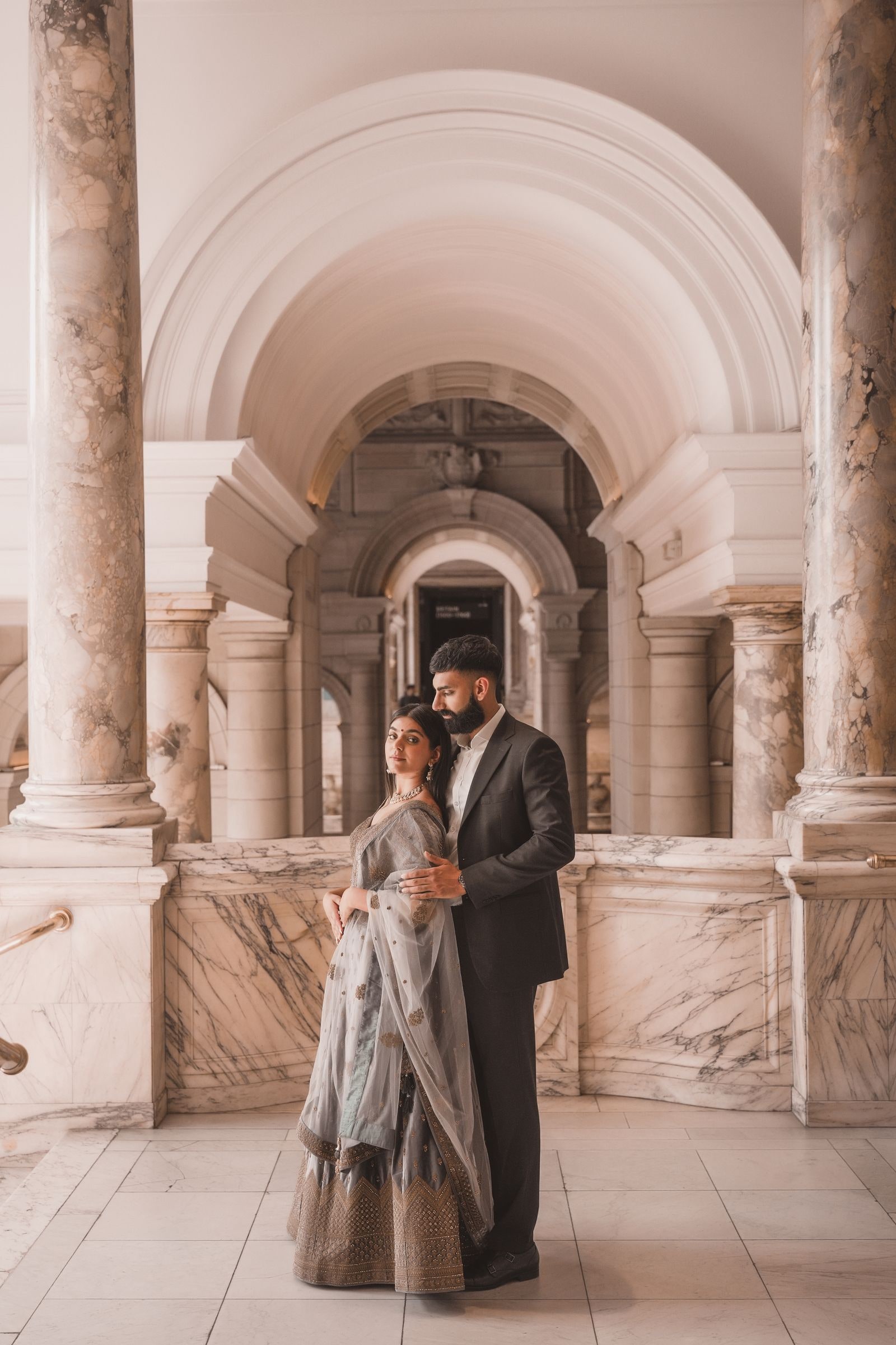 Couple holding each other beneath a marble arch in the museum corridor