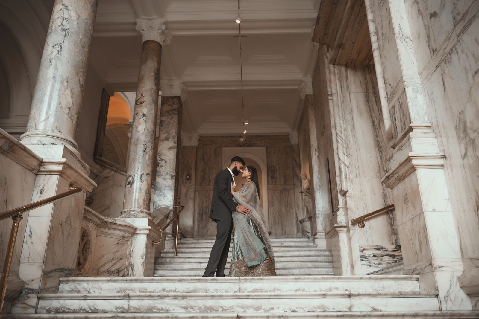 Couple embracing at the foot of the marble stairs, columns framing them