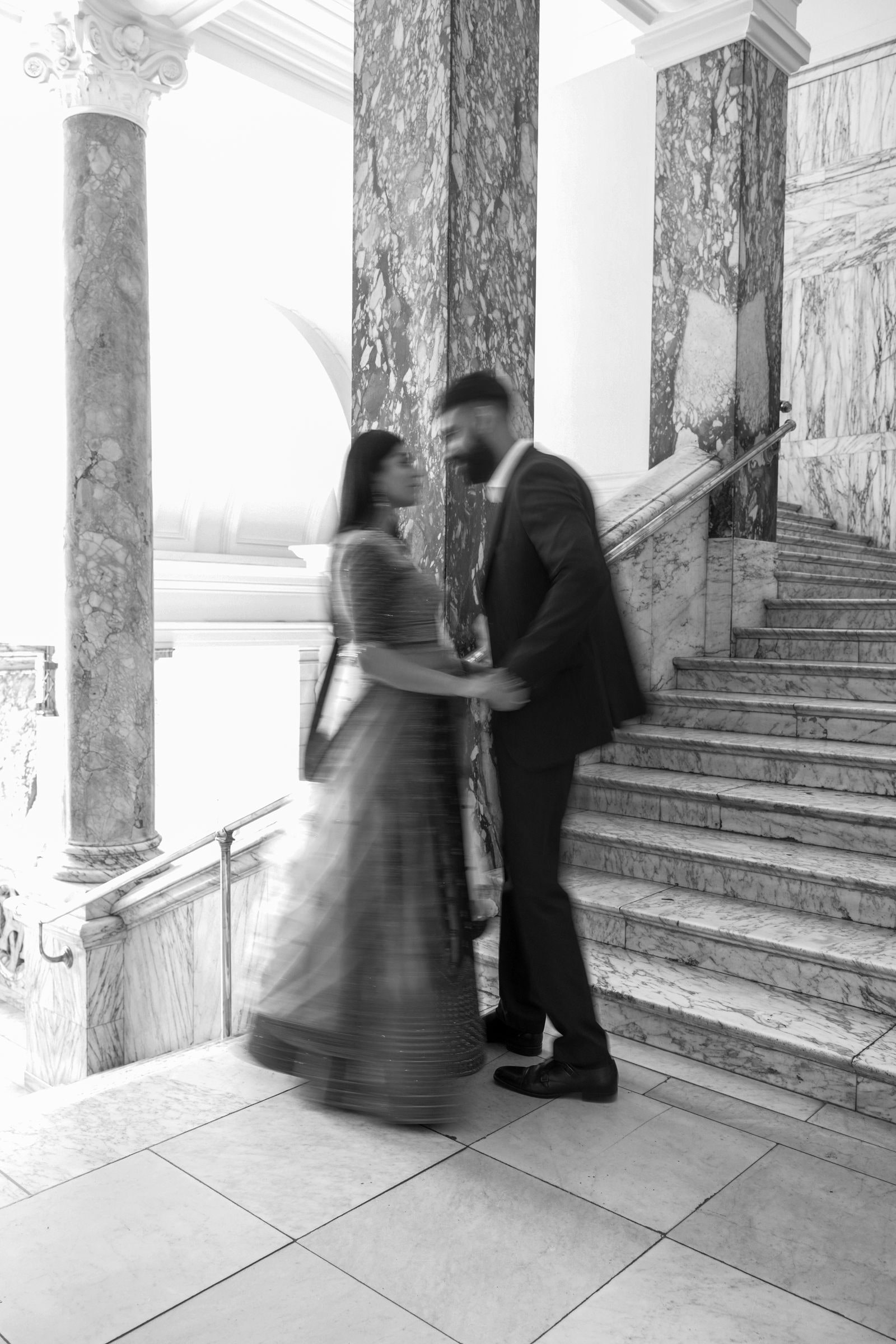 Couple on the museum stairs, her lehenga blurred with movement, in black and white