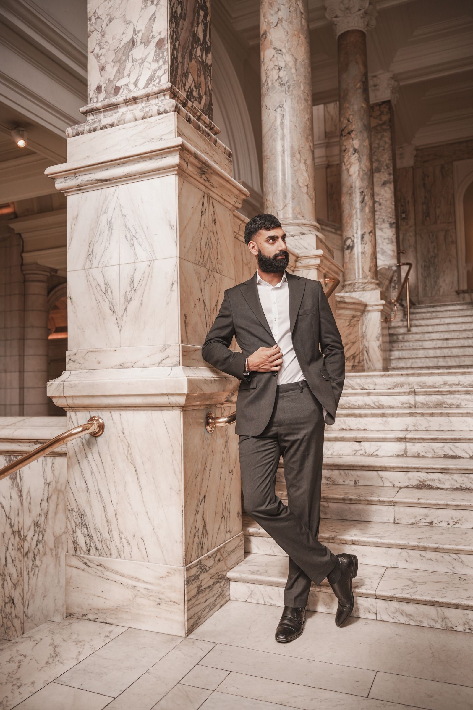 Man in a dark suit leaning against a marble pillar by the staircase