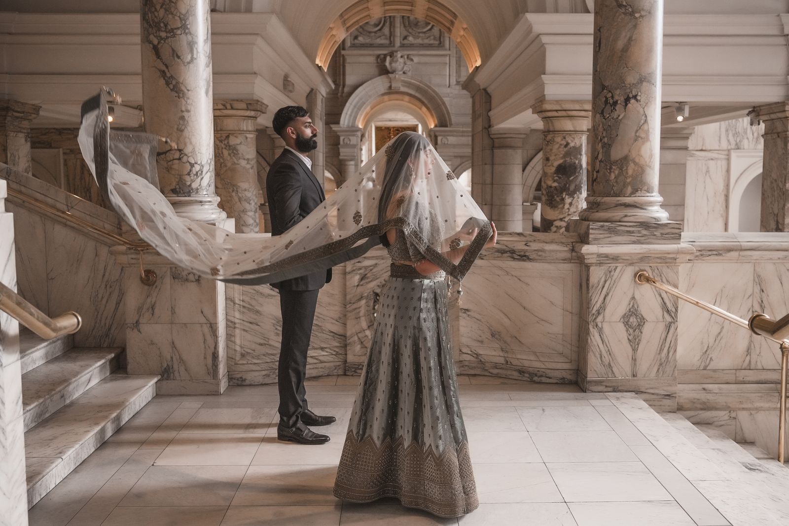 Couple on a marble staircase, her dupatta caught in the air behind her