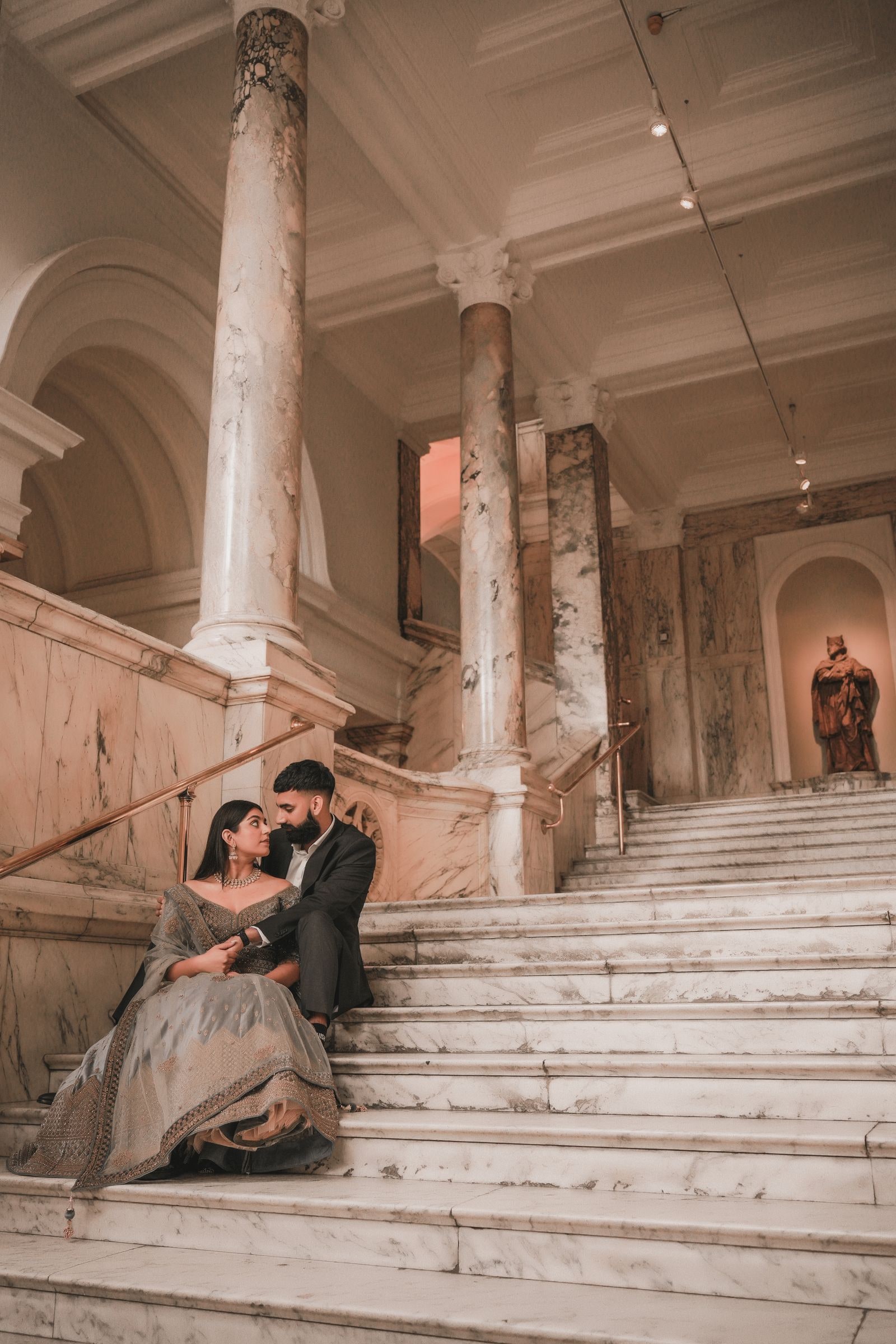 Couple sitting on the wide marble staircase, columns and arches rising above